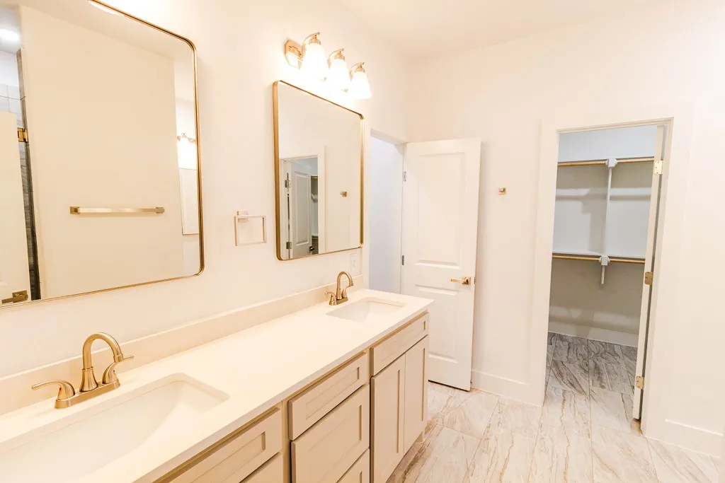 Dual vanity with undermount sinks, light-toned cabinetry, and brushed gold fixtures