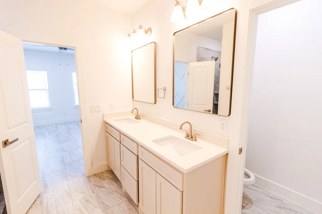 Spa-inspired dual-sink vanity featuring a continuous quartz countertop, soft-close cabinetry with wood-finish detailing, and brass-finish faucets