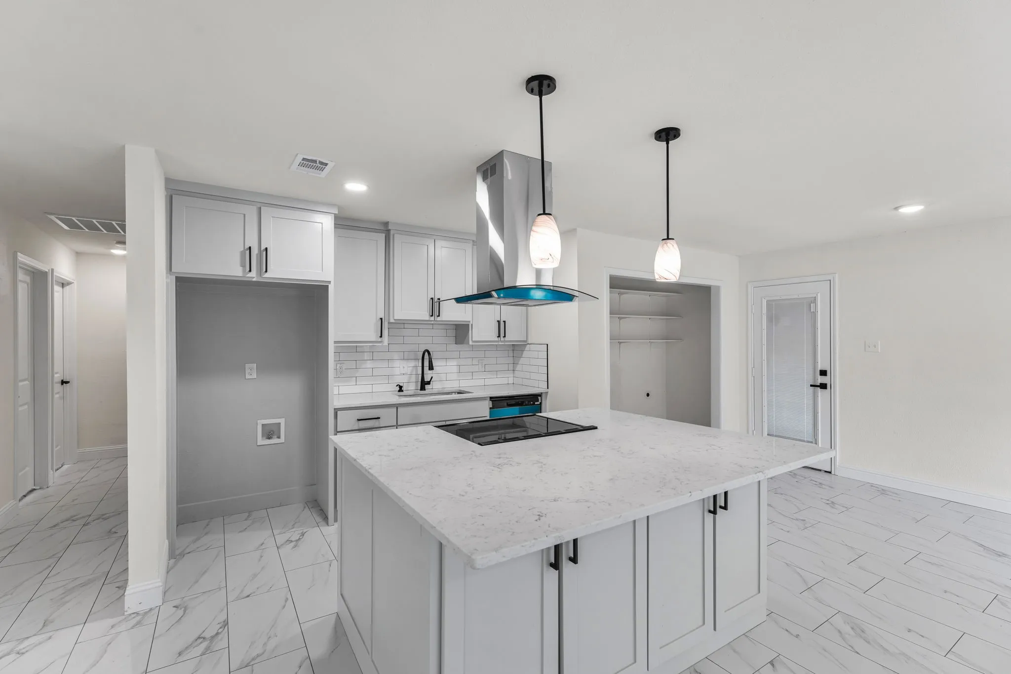 Contemporary kitchen featuring a large island with an integrated cooktop, pendant lighting, light gray cabinetry, and a subway tile backsplash