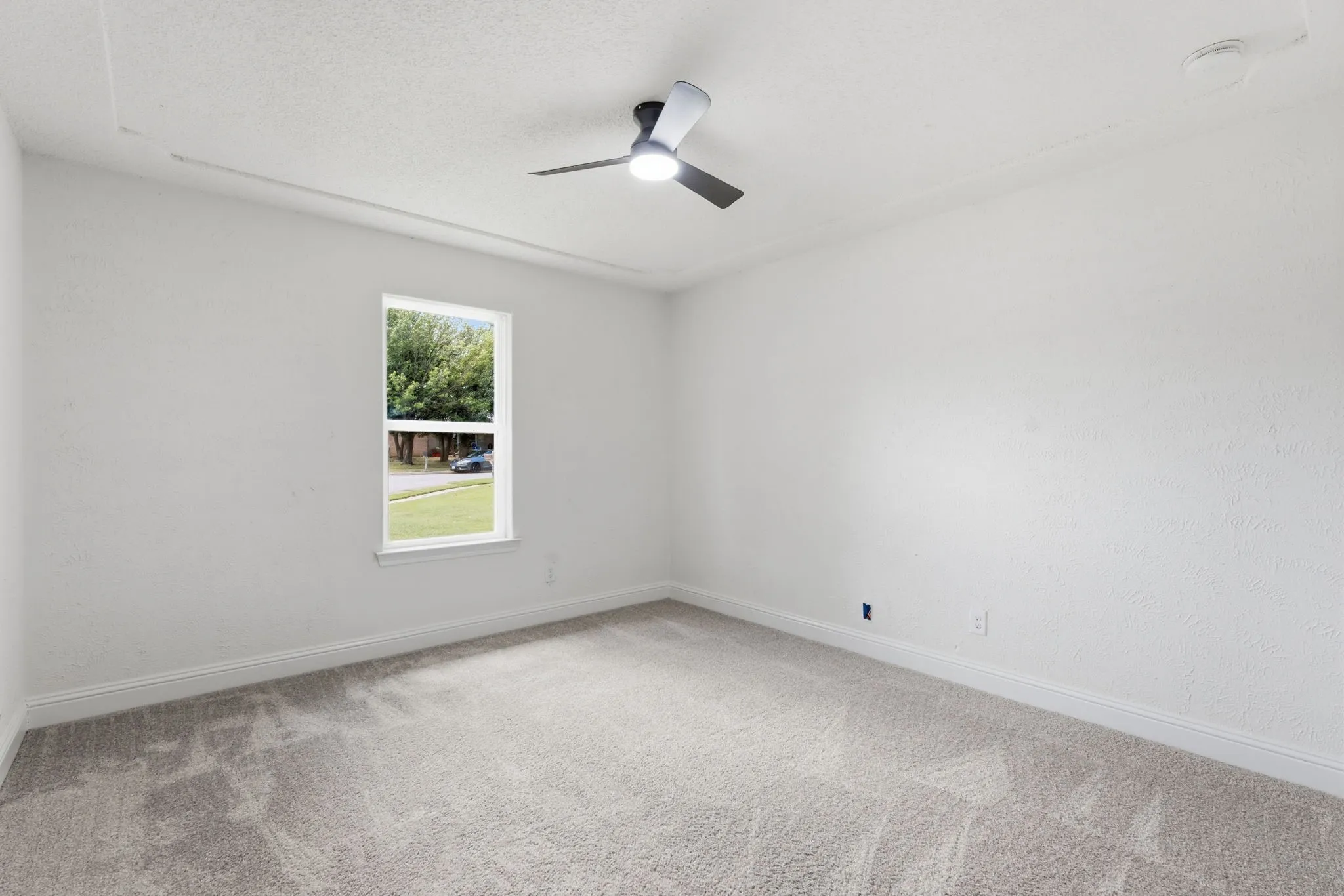 Spacious room featuring neutral carpeting, white textured walls, and a window offering natural light