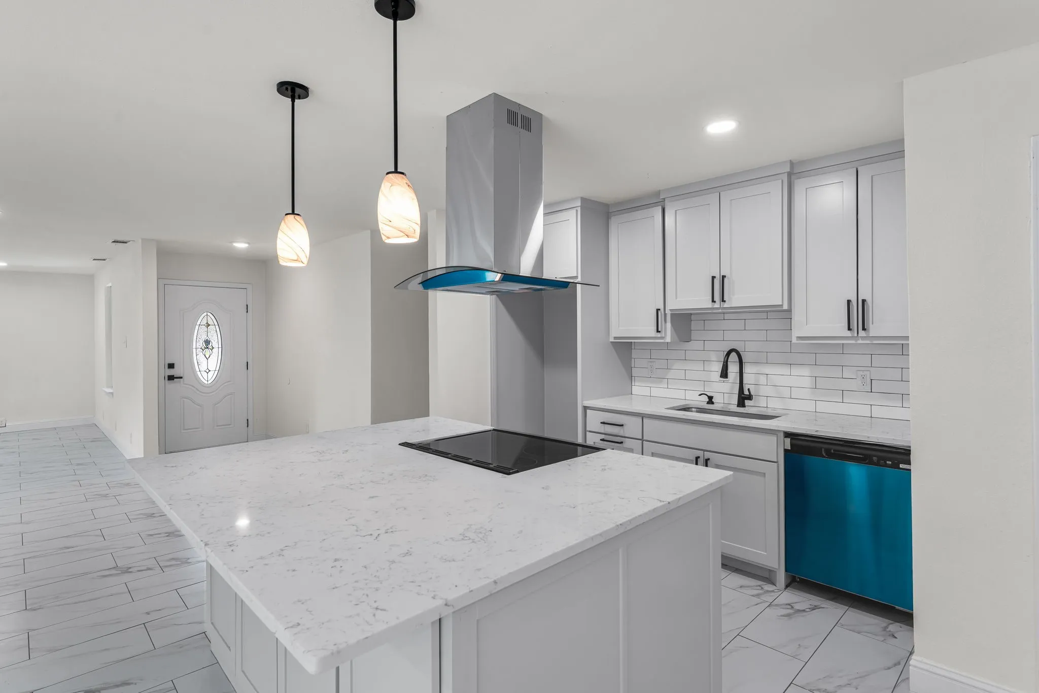Contemporary kitchen featuring a large island with an integrated cooktop, pendant lighting, white shaker cabinetry, and a subway tile backsplash
