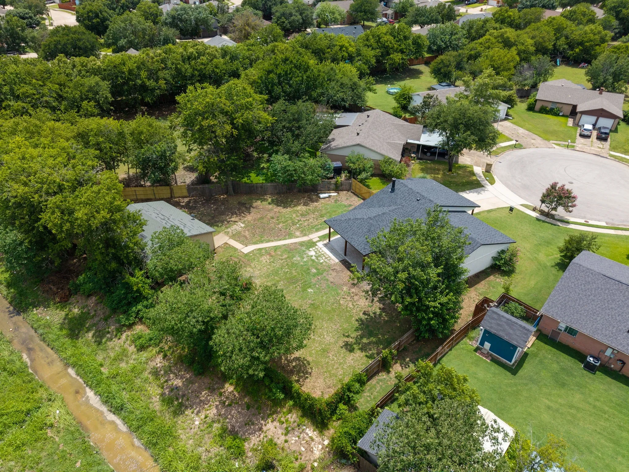 Aerial perspective showcasing a residential property with a dark shingle roof and a covered patio