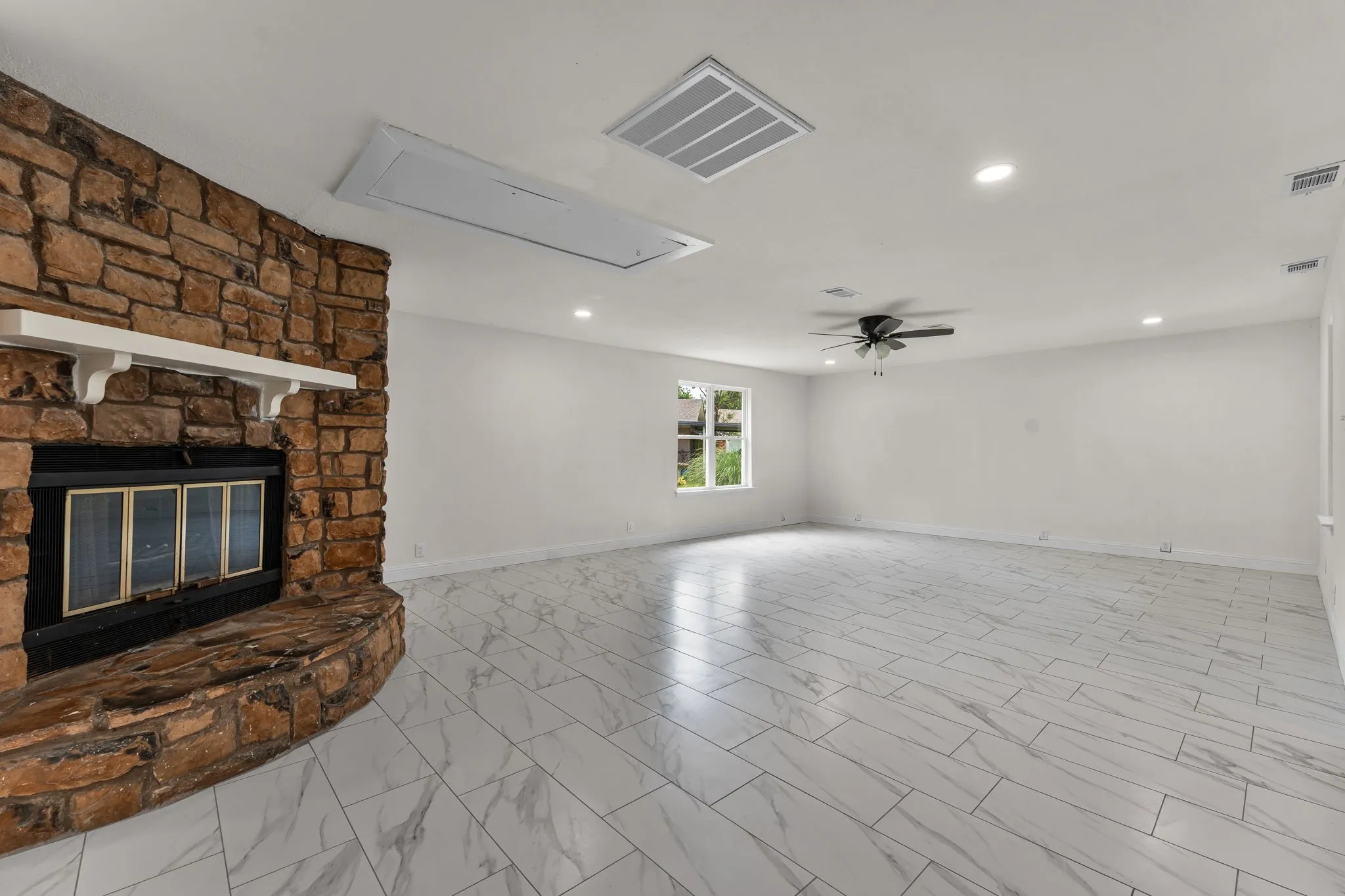 Spacious interior featuring a stone fireplace with a white mantel, white walls, and large format marble-look tile flooring