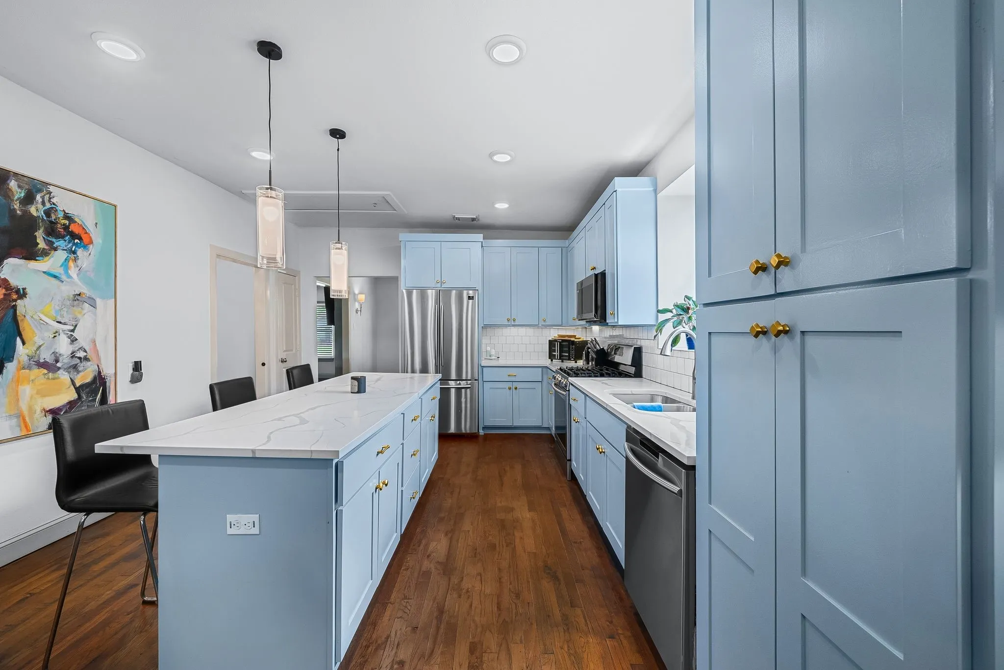 Kitchen featuring an expansive center island with seating, light blue cabinetry with gold-tone hardware, wood-finish flooring, and recessed lighting