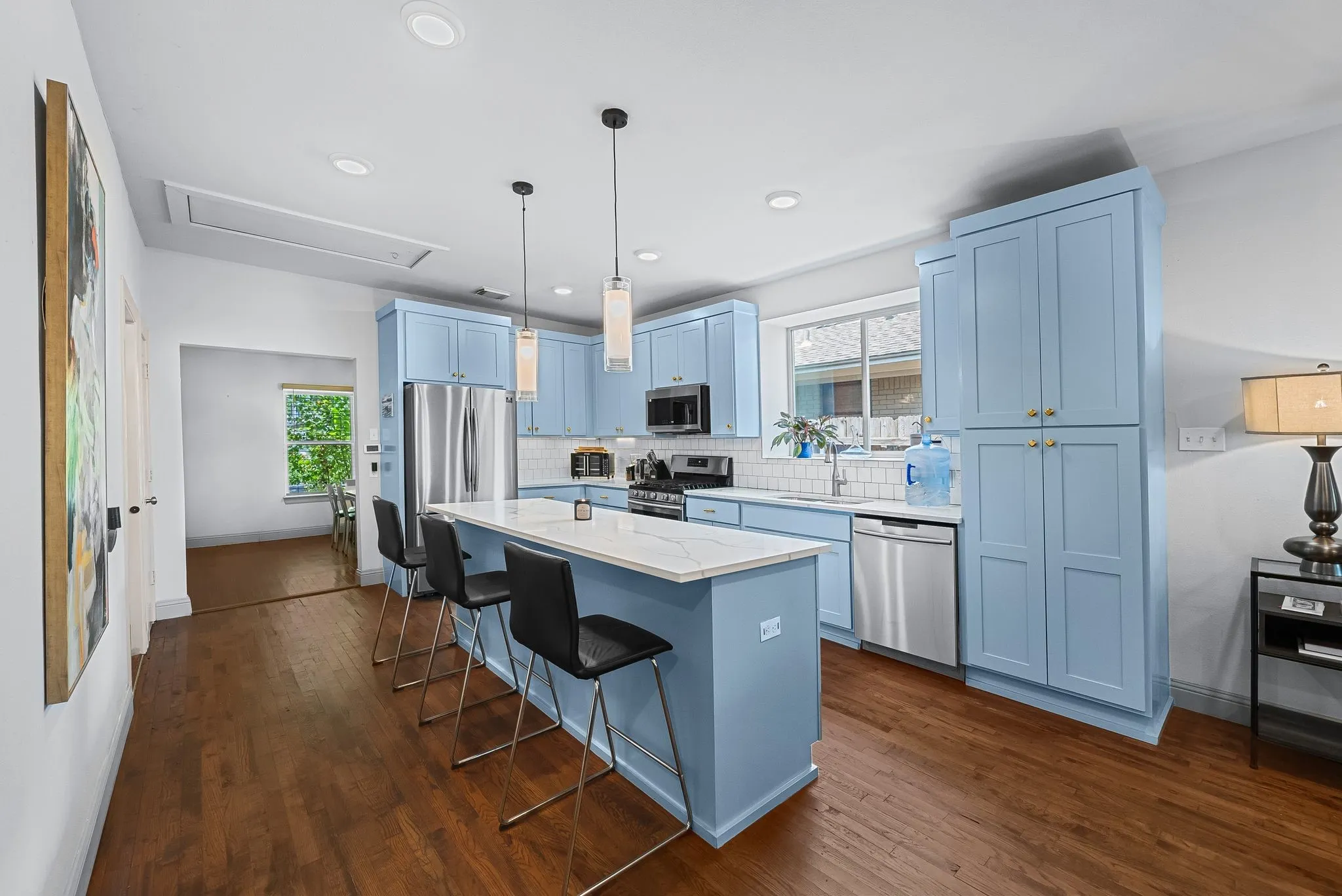 Well-appointed kitchen featuring light blue cabinetry, stainless steel appliances, a white tile backsplash, and a central island with countertop seating