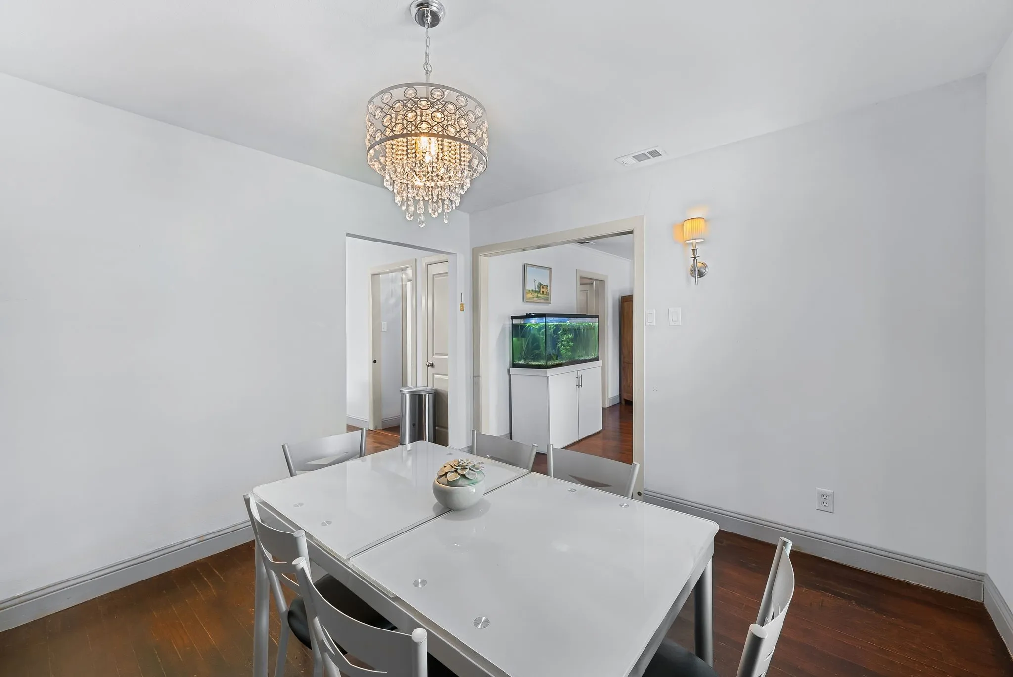Dining area featuring an ornate crystal chandelier, recessed wall sconce, and dark wood-finish flooring
