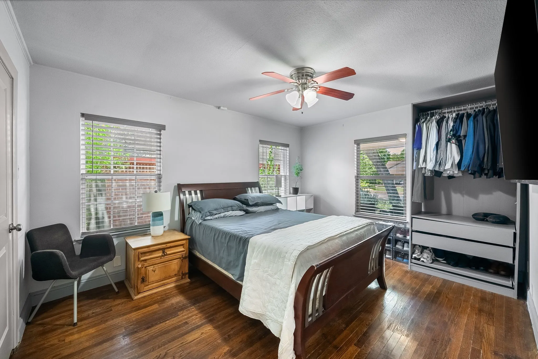 Bedroom featuring rich wood-finish flooring, a ceiling fan with light fixture, and multiple windows with blinds