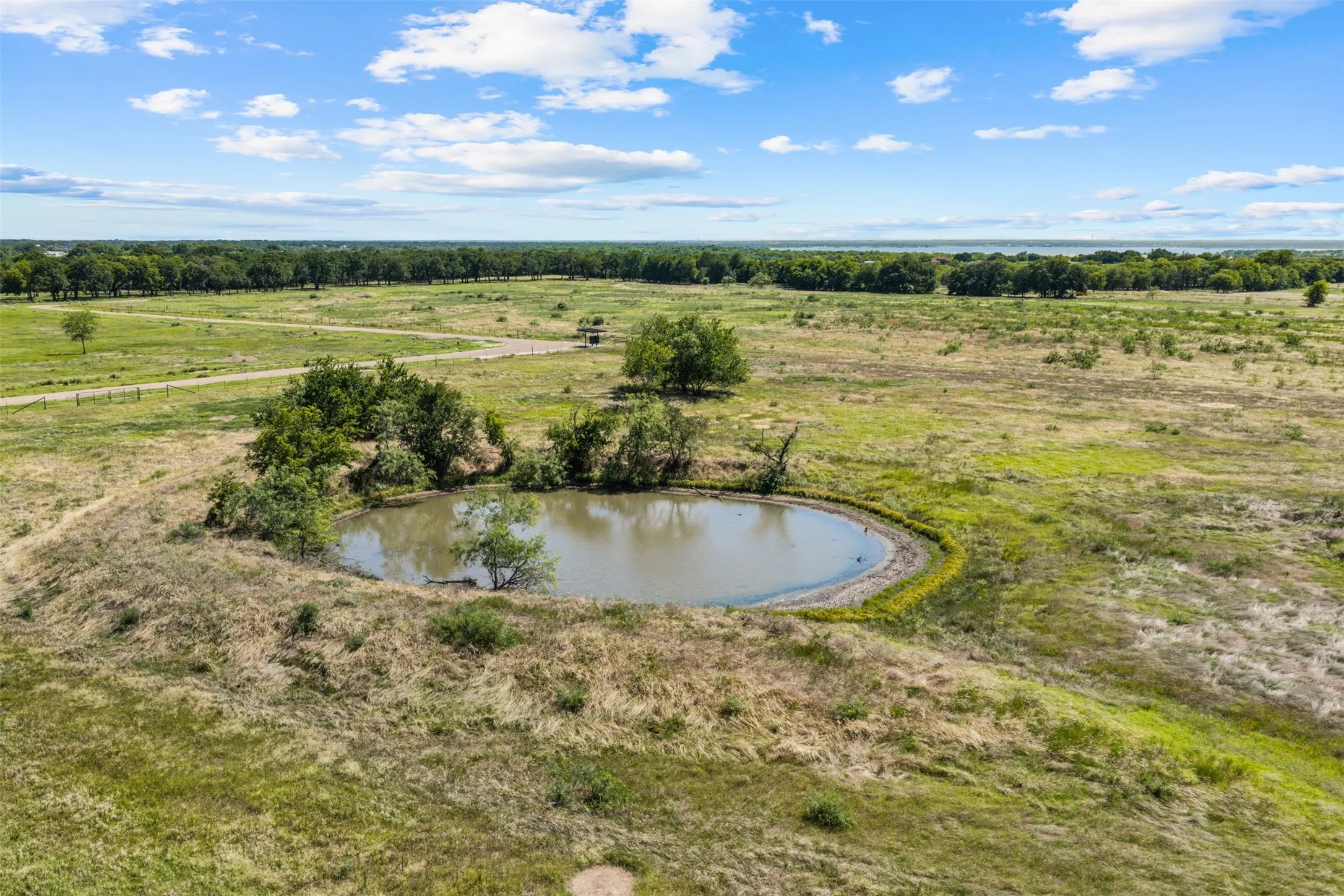 Expansive parcel featuring a large pond and mature trees, surrounded by open grasslands and distant tree lines