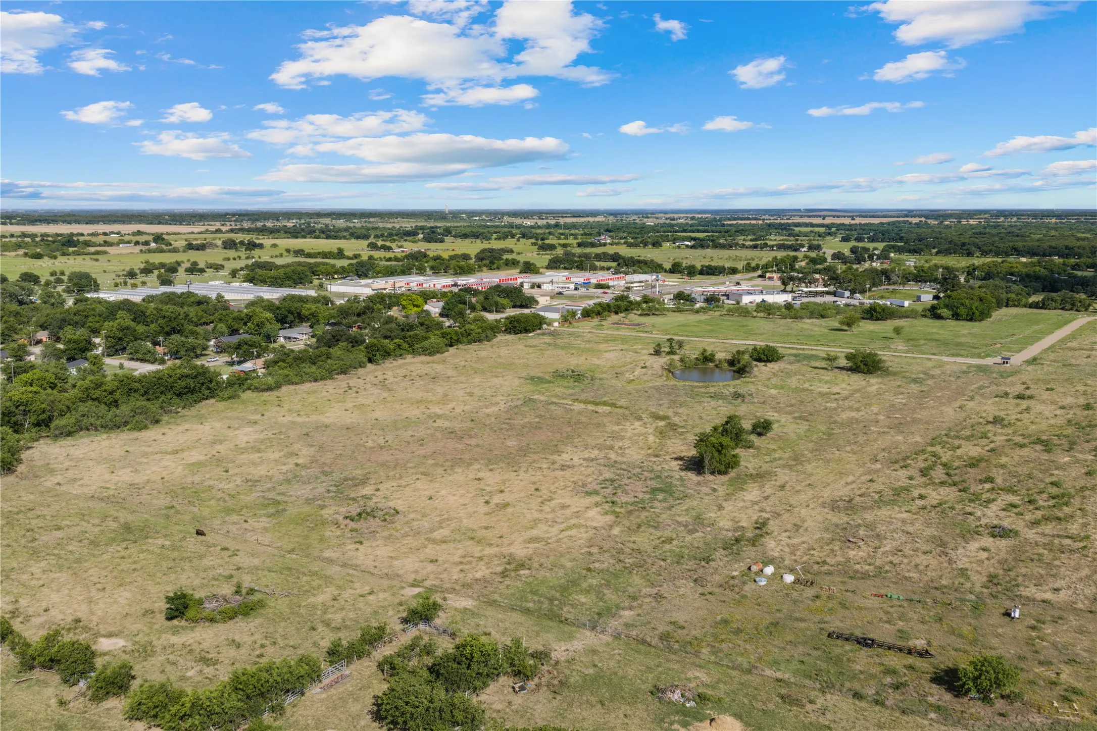 Expansive land parcel featuring open fields, scattered mature trees, and a visible pond