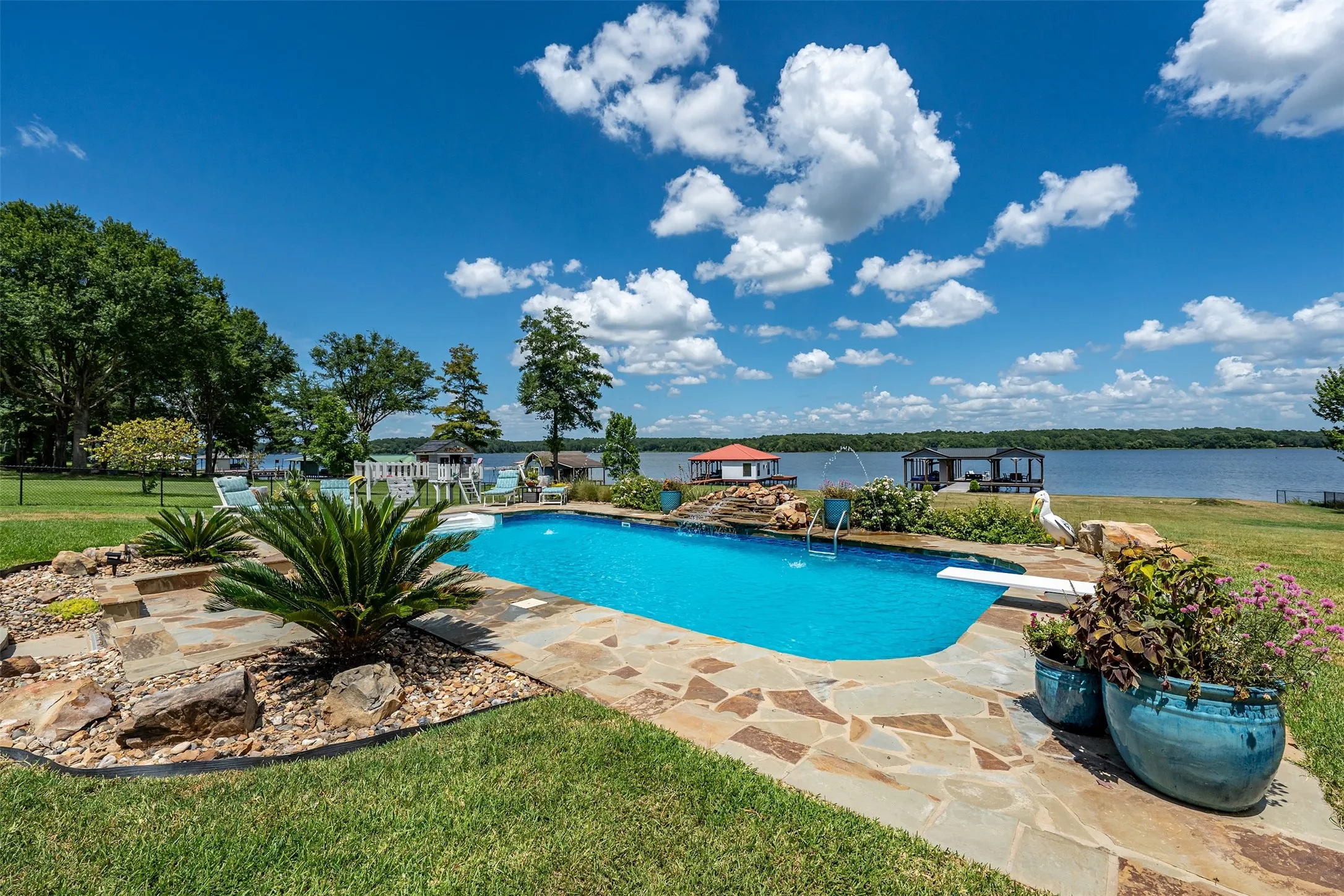 Waterfront property featuring an in-ground swimming pool with flagstone surround, diverse landscaping, and direct access to the lake