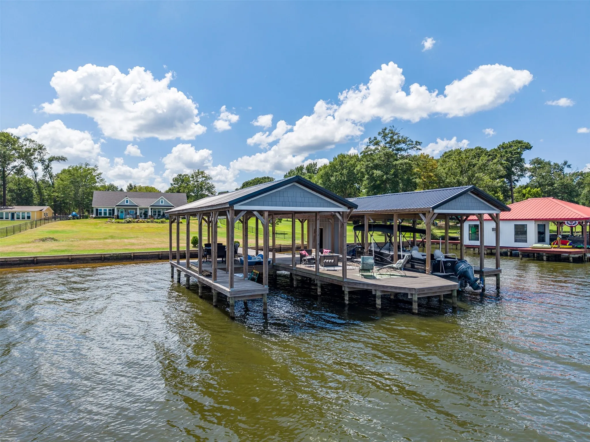Expansive multi-slip boat dock featuring covered boat berths, open-air seating areas, and a separate covered boathouse with a red metal roof