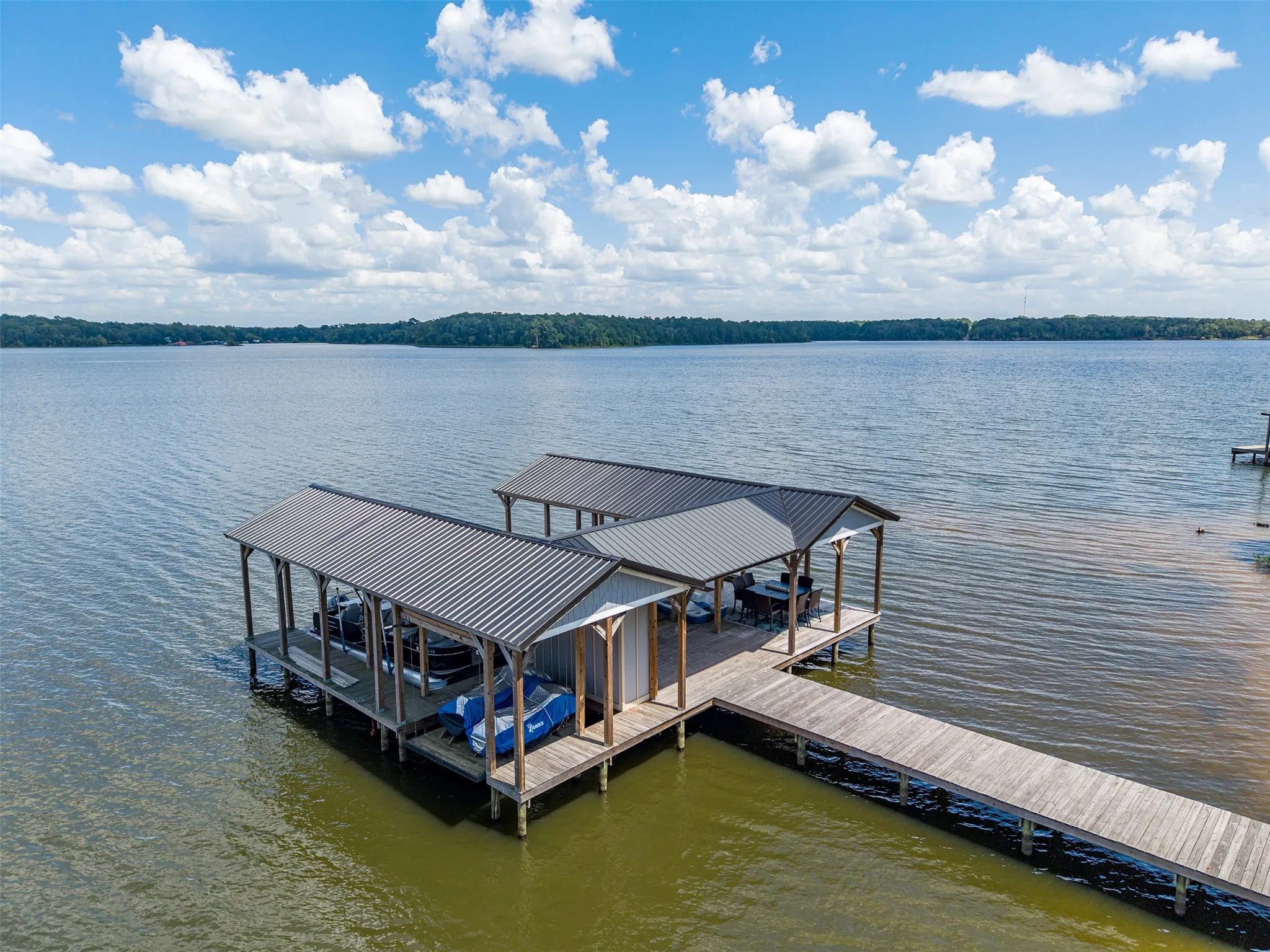Private dock with two covered boat slips featuring metal roofs and a long wood-finish walkway