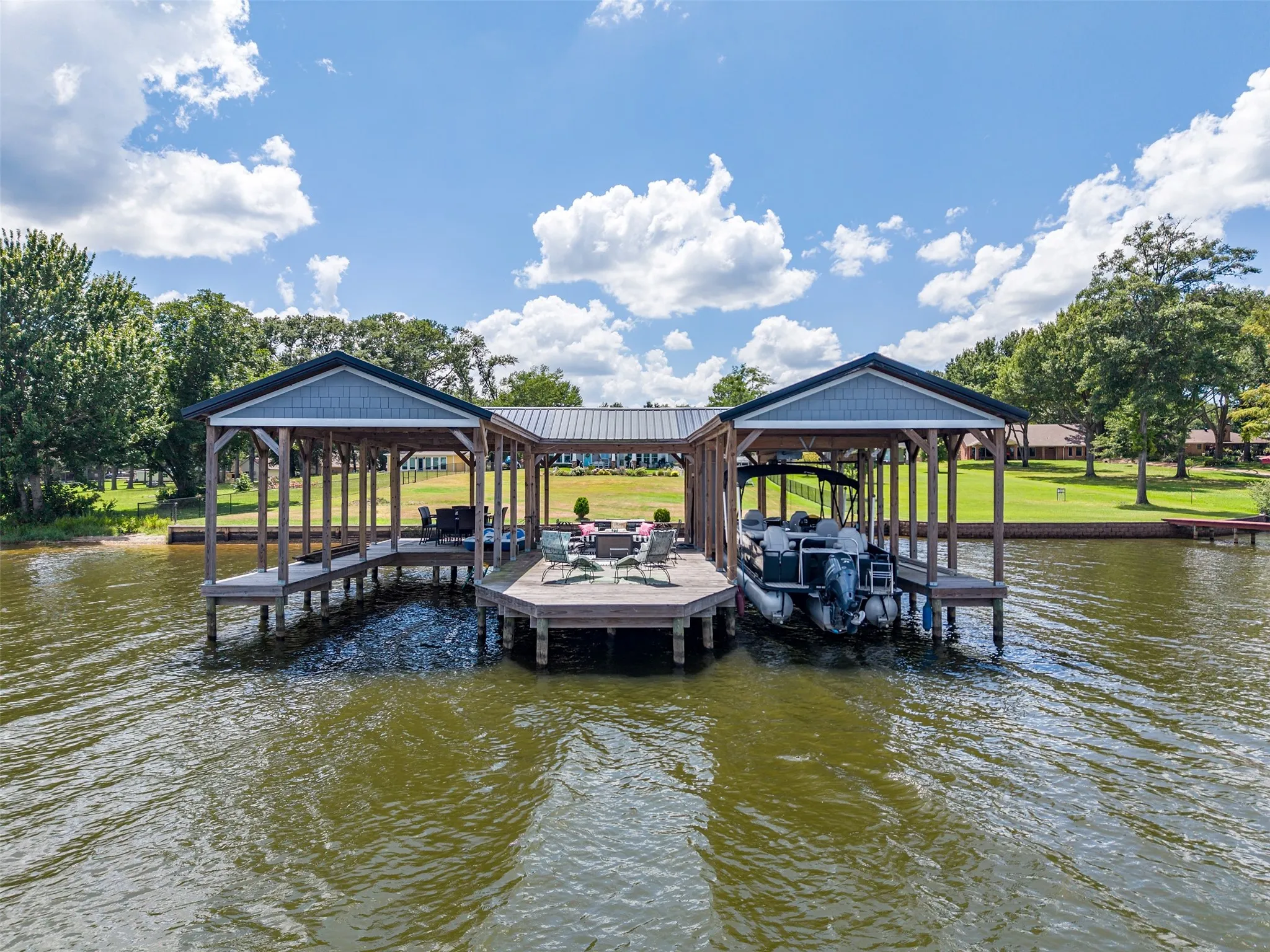 Expansive double boat dock featuring two covered slips, a central open deck area, wood pilings, and a metal roof