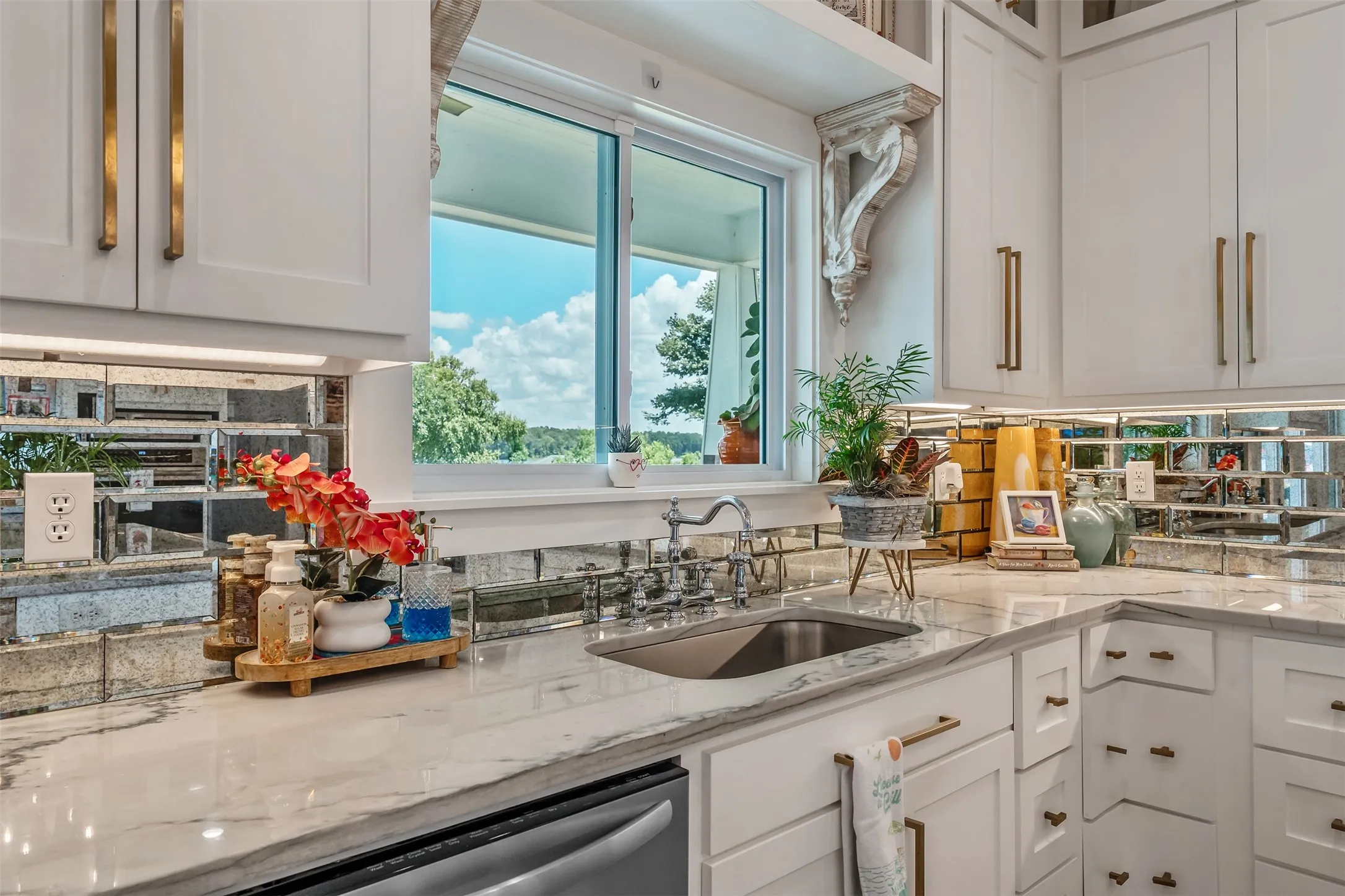 White cabinetry with brass hardware, a polished sink, stone countertops, and a mirrored subway tile backsplash