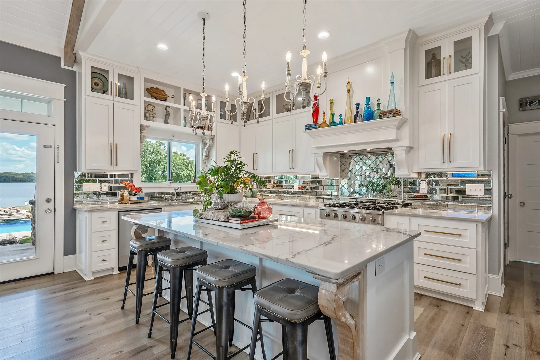 Gourmet kitchen featuring a large island with a waterfall edge, a professional-grade gas range, custom white cabinetry, a mirrored tile backsplash, and wood-finish flooring