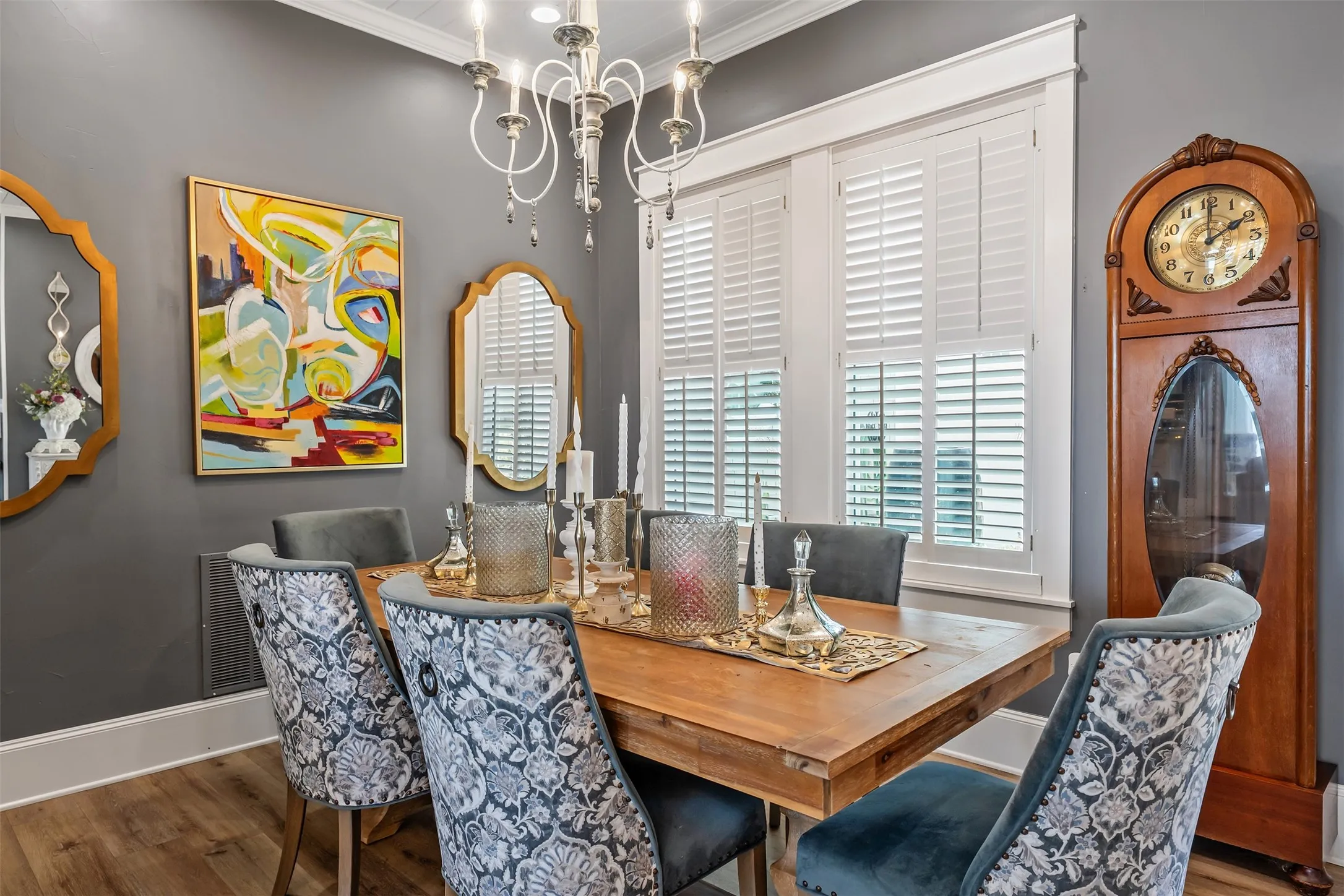 Dining space featuring wood-finish flooring, a white chandelier, crown molding, and white plantation shutters on the windows