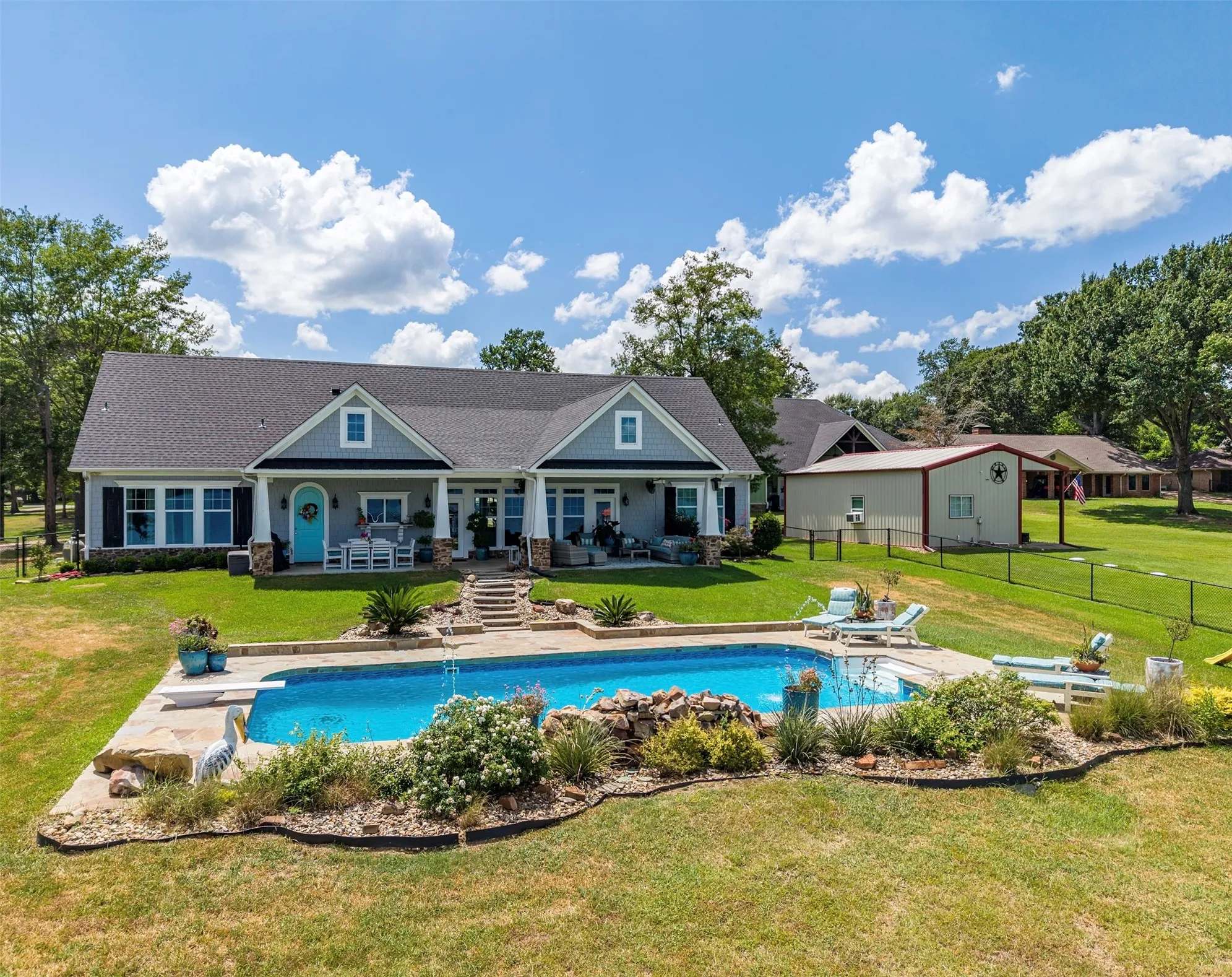 Rear exterior showcasing a large inground swimming pool with integrated rock features, an expansive concrete patio, and a diving board