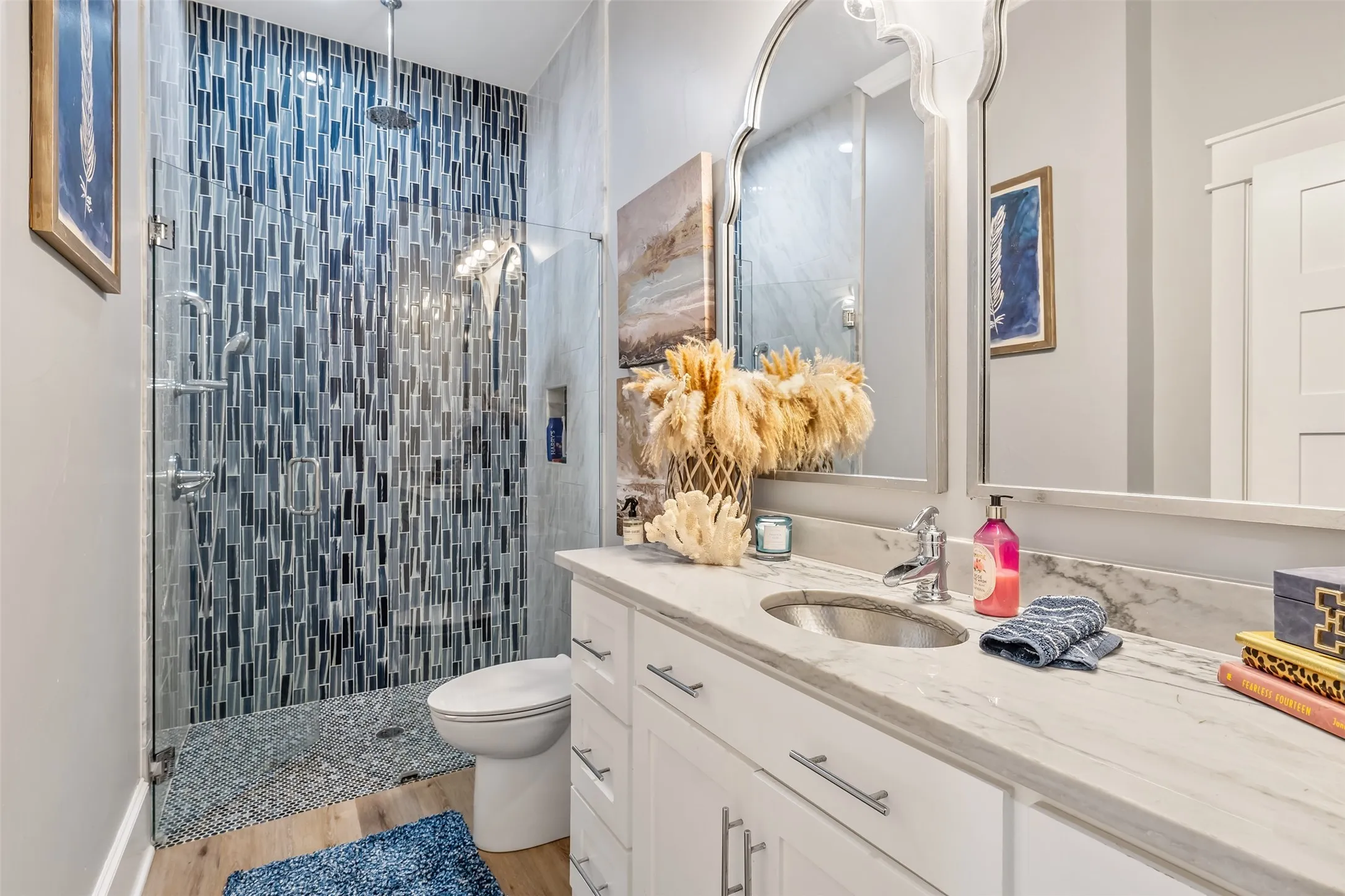 Glass-enclosed shower featuring blue and gray mosaic tile, rain shower head, and polished chrome fixtures