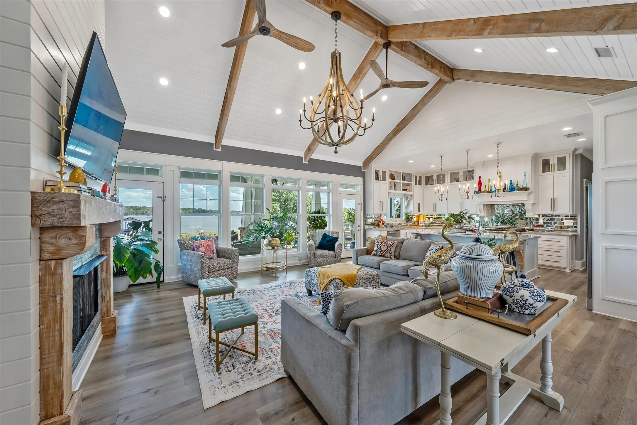 Open-concept living space featuring vaulted ceilings with exposed wood beams, a rustic wood mantel fireplace, wood-finish flooring, and a wall of windows