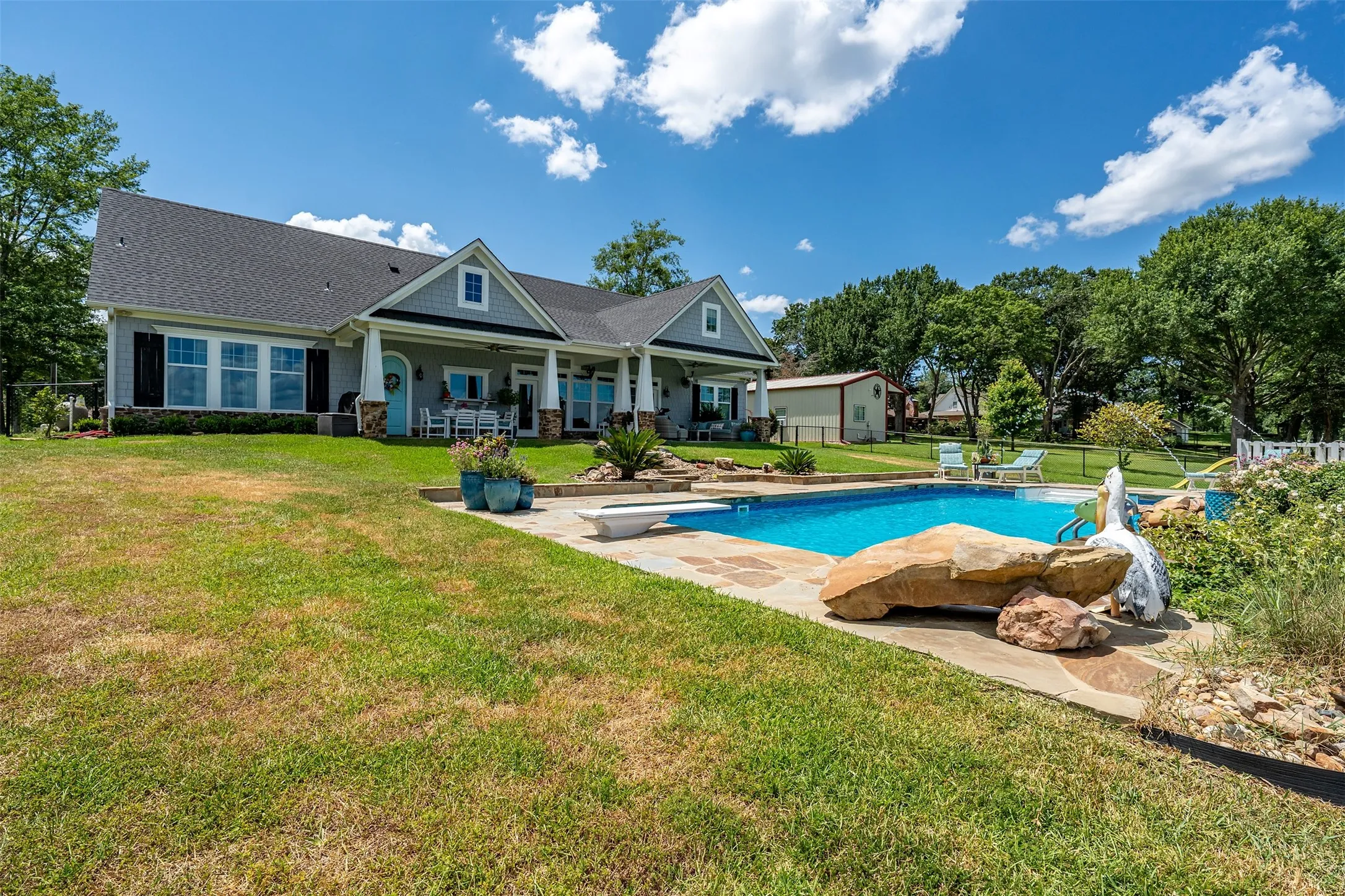 Expansive backyard featuring a rectangular swimming pool with integrated diving board, flagstone coping, and surrounding flat stone patio