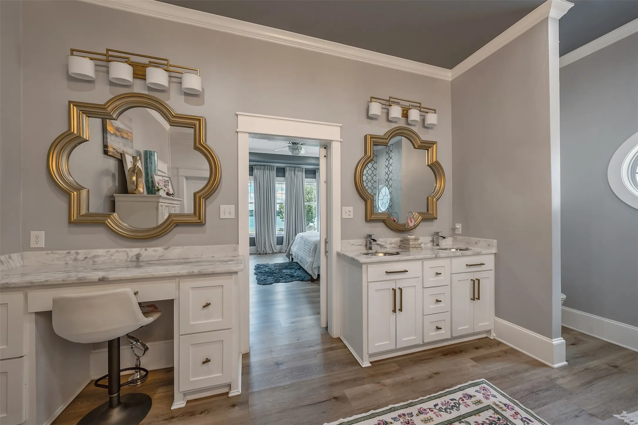 Bathroom featuring dual white vanity cabinets, stone countertops, gold-framed mirrors, and wood-finish flooring