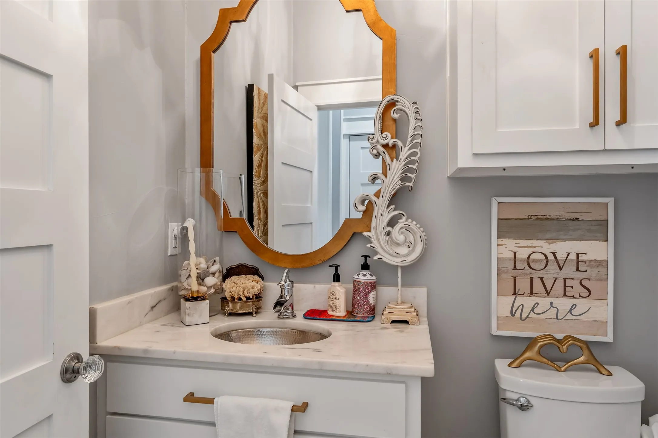 Bathroom vanity featuring a hammered metal sink, stone countertop, white shaker-style cabinetry, and a decorative gold-framed mirror