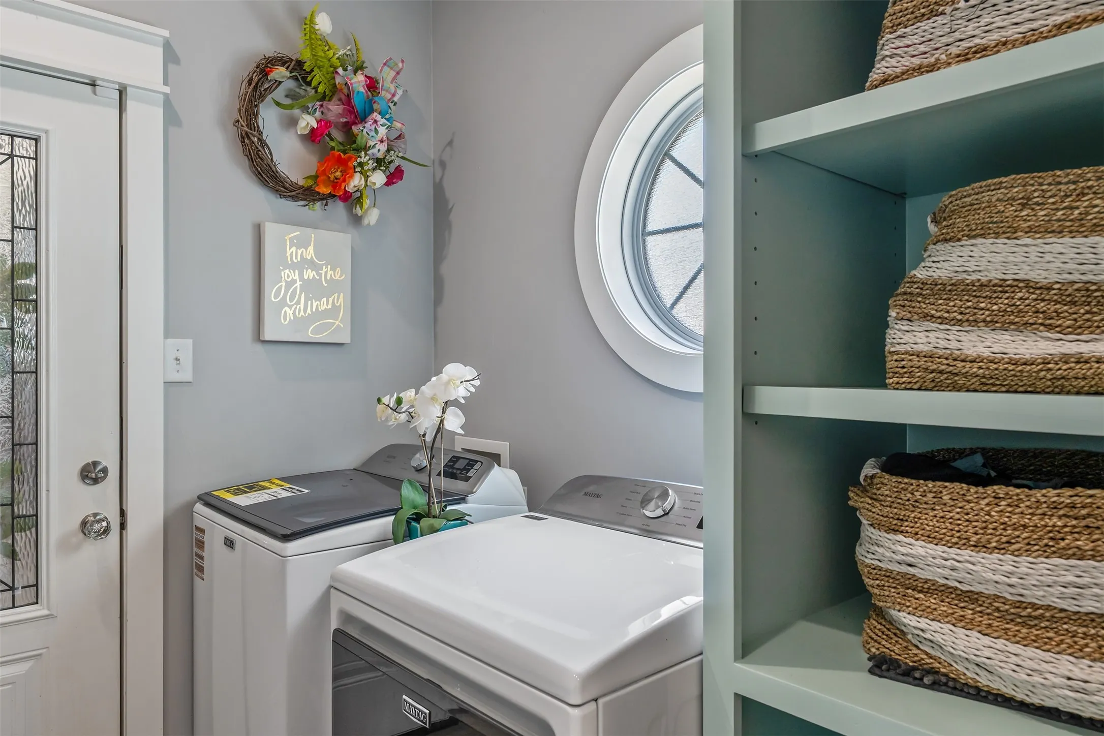 Dedicated laundry area featuring a full-light entry door with decorative glass, a prominent round window, and built-in shelving