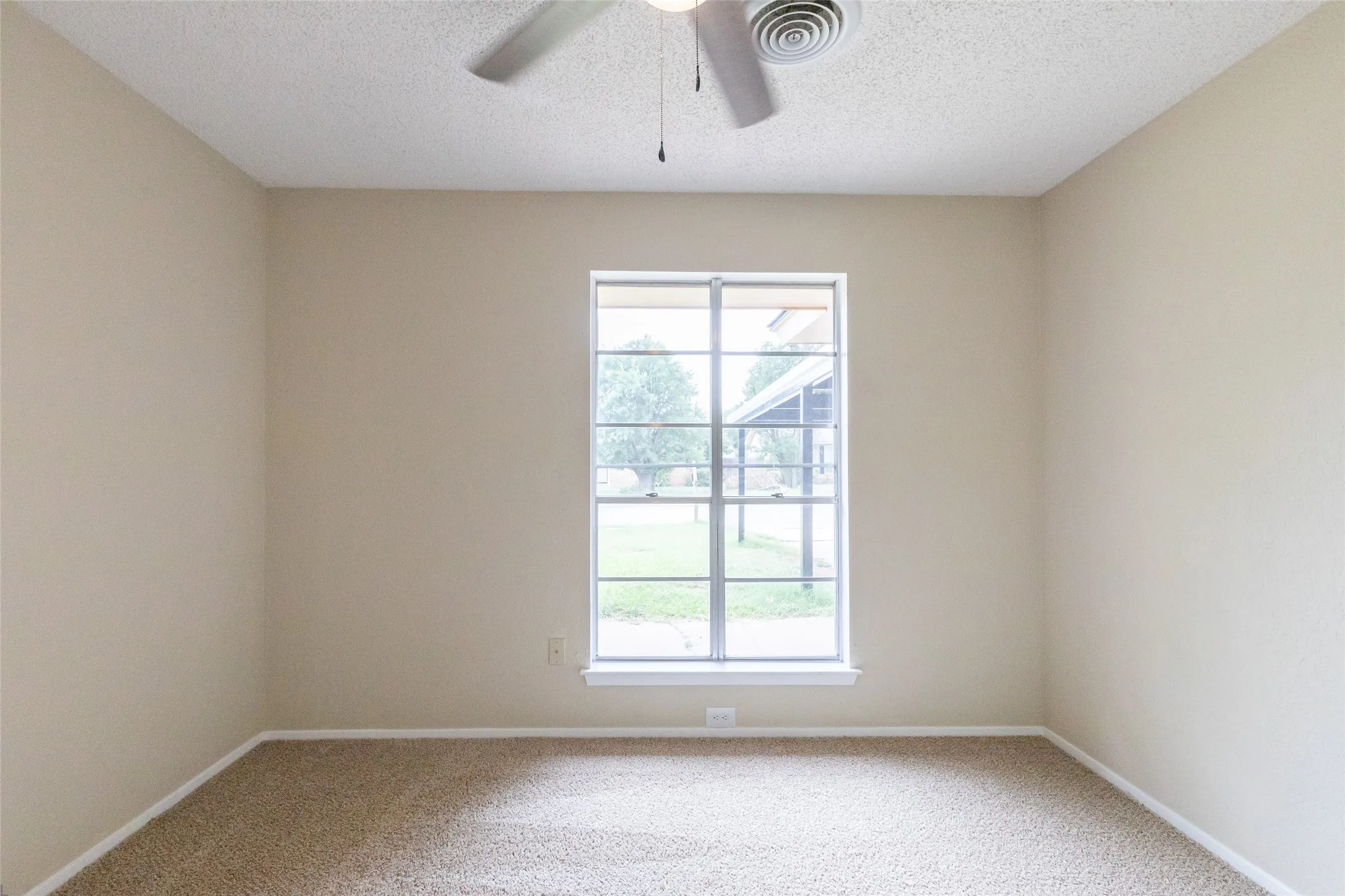Bedroom featuring a window with grid detailing, neutral carpet flooring, light beige wall paint, white baseboards, and a ceiling fan