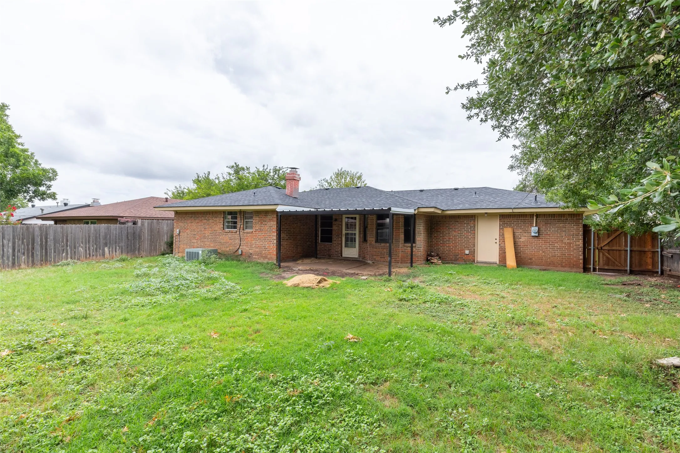 Rear exterior showcasing a brick facade, covered patio area, and a wood privacy fence