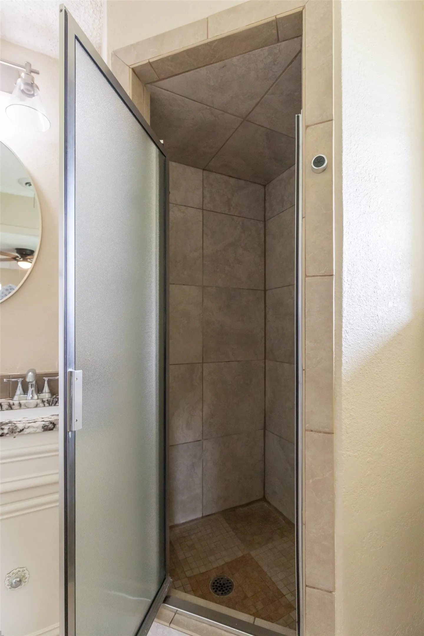 Walk-in shower with tiled walls and floor, featuring a frosted glass door