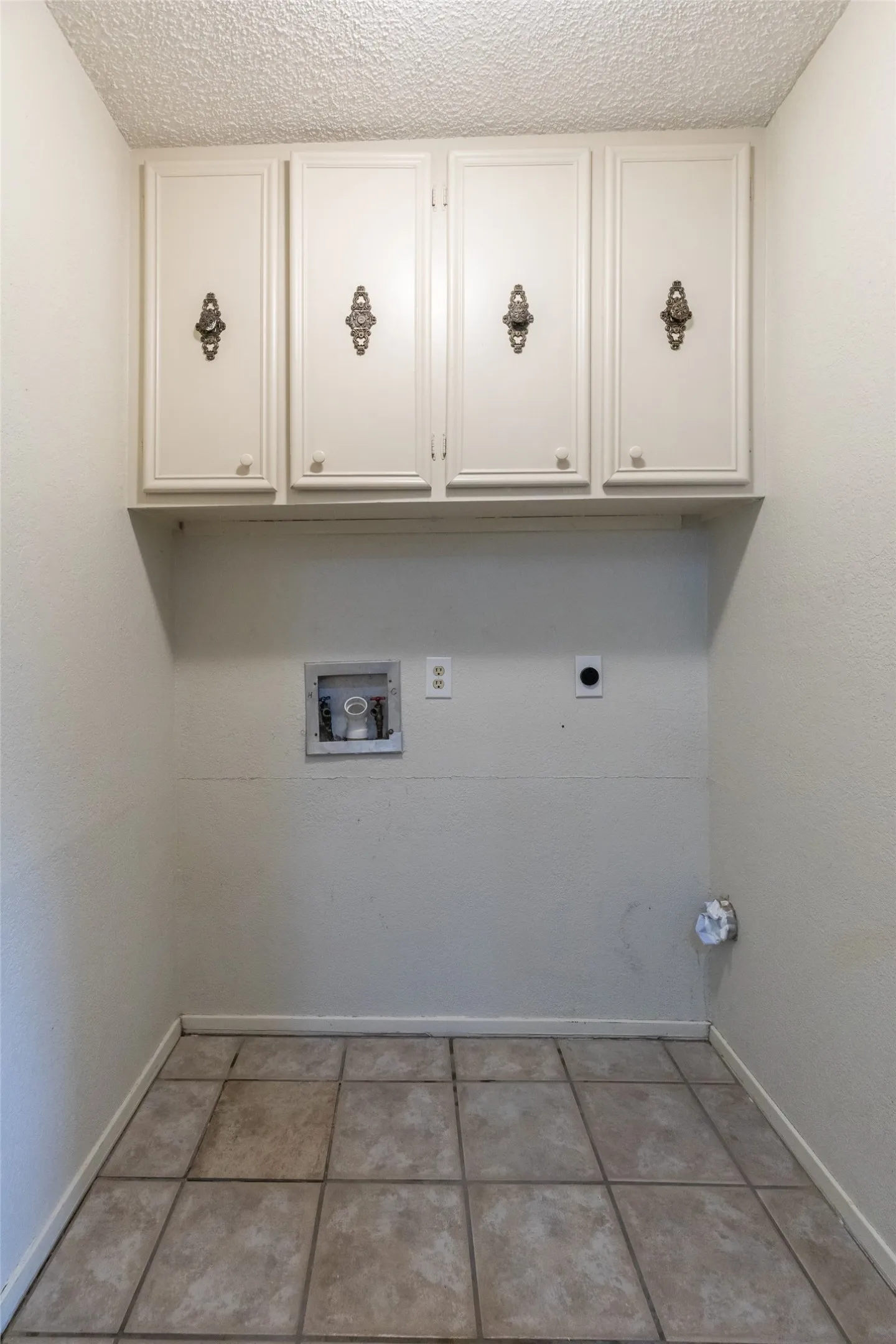 Utility area featuring four upper cabinets with decorative hardware, a built-in shelf, tile flooring, and textured ceilings