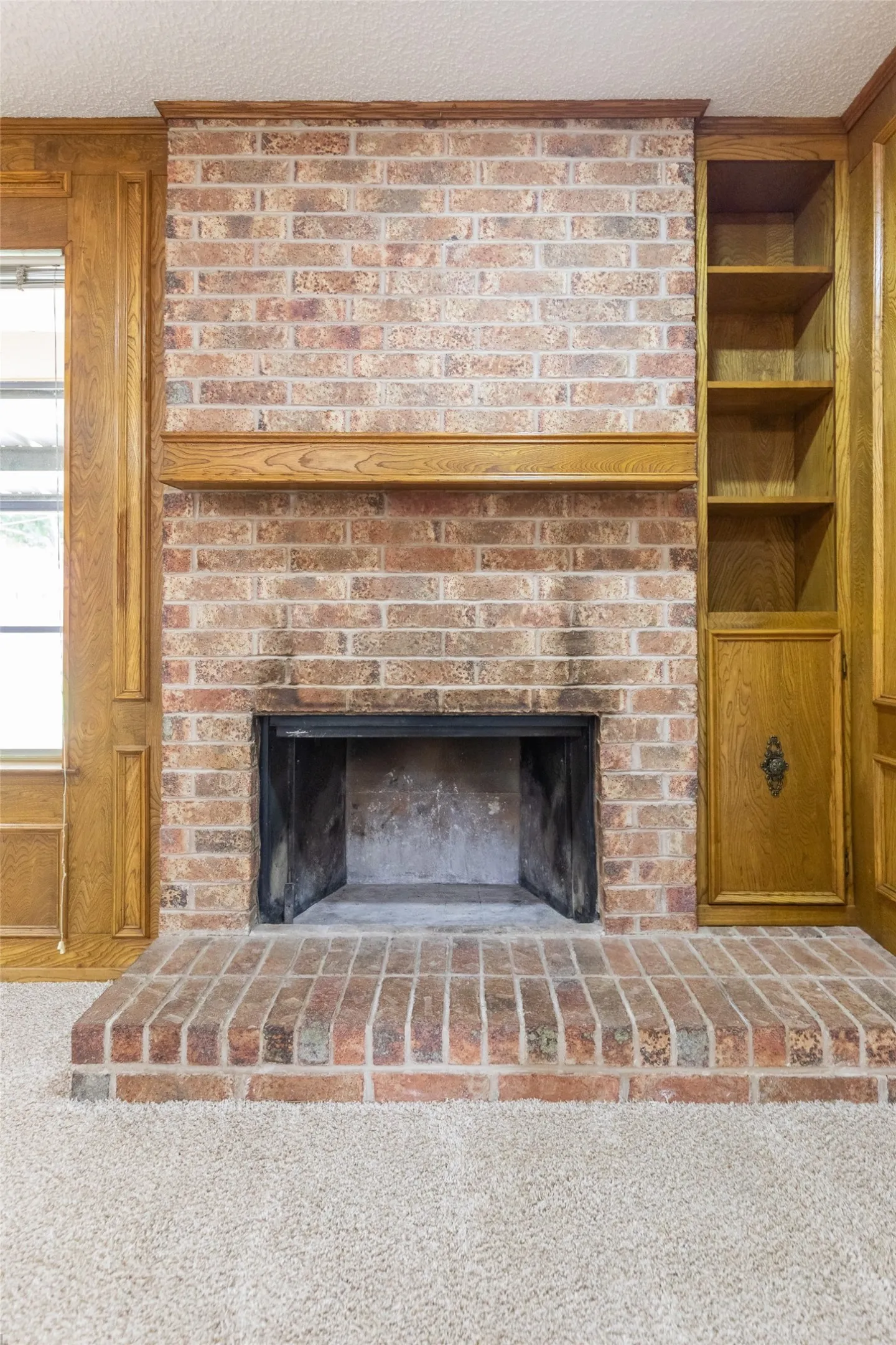 Brick fireplace with a raised hearth, wood mantel, and integrated built-in shelving