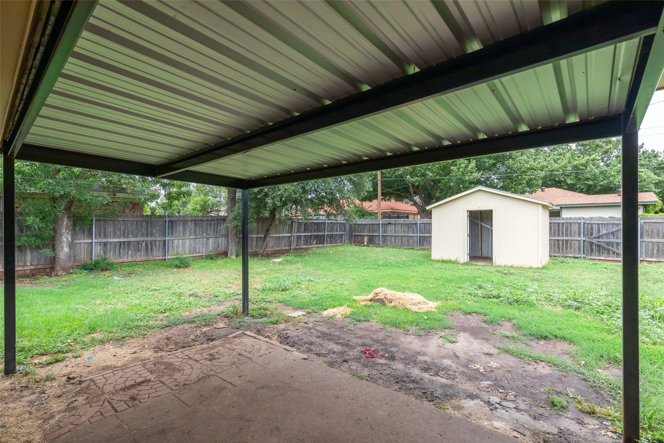 Expansive backyard featuring a covered patio with a metal roof, a wood fence surrounding the perimeter, and a detached storage shed