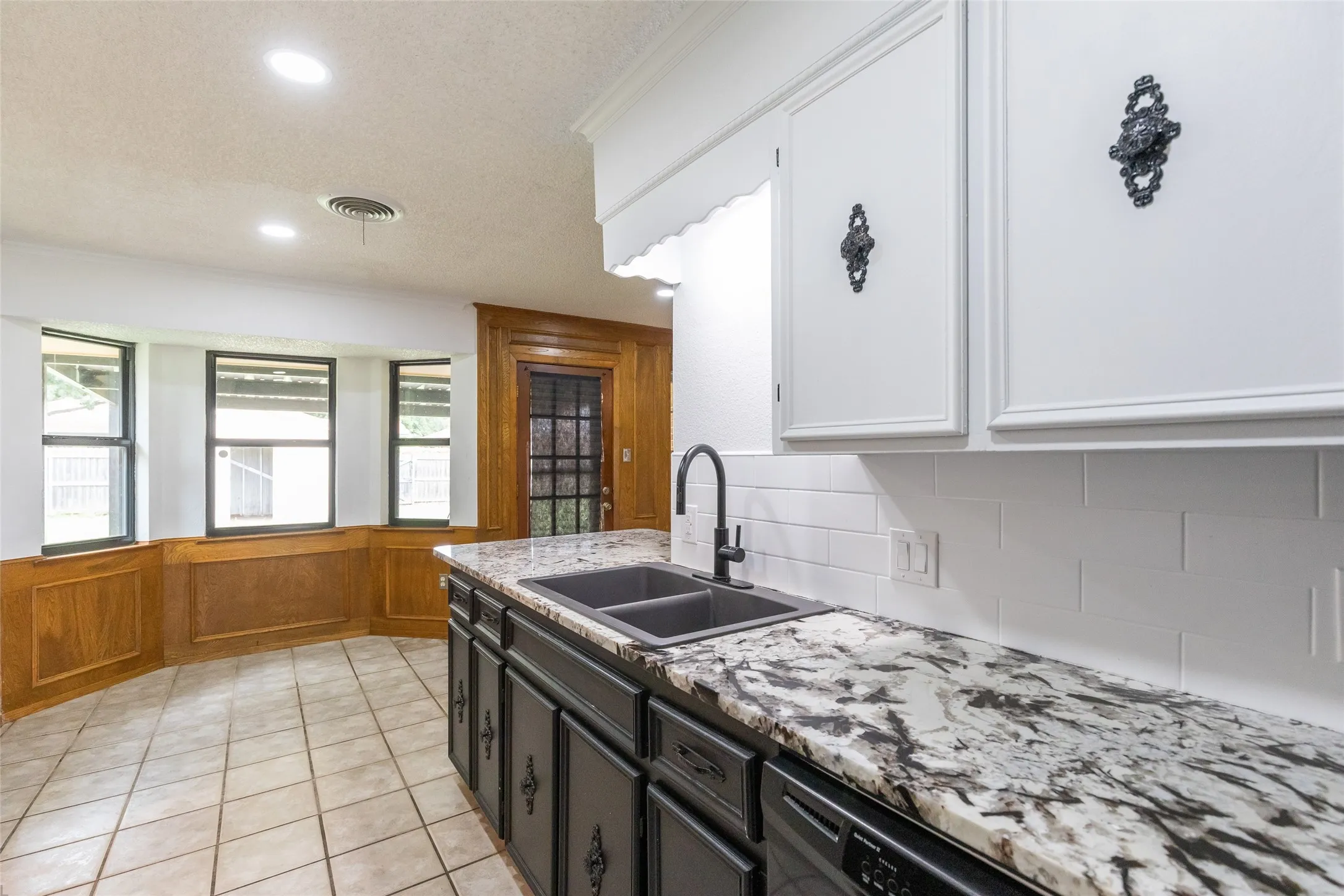 Kitchen featuring white upper cabinetry with ornate hardware, dark lower cabinetry, and a light-toned countertop with dark veining