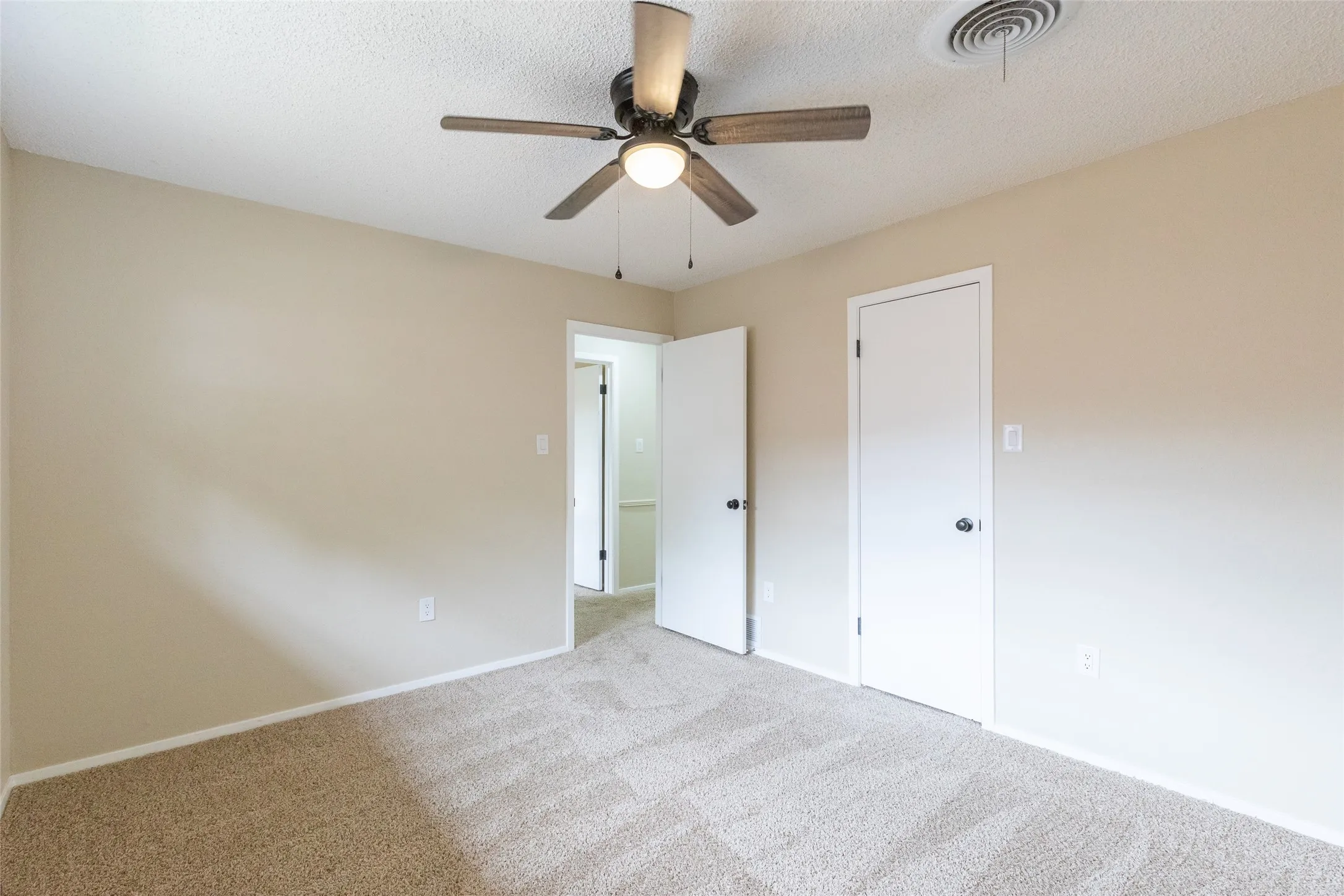 Neutral-toned carpeted interior space featuring a ceiling fan with light, white trim, and two white interior doors