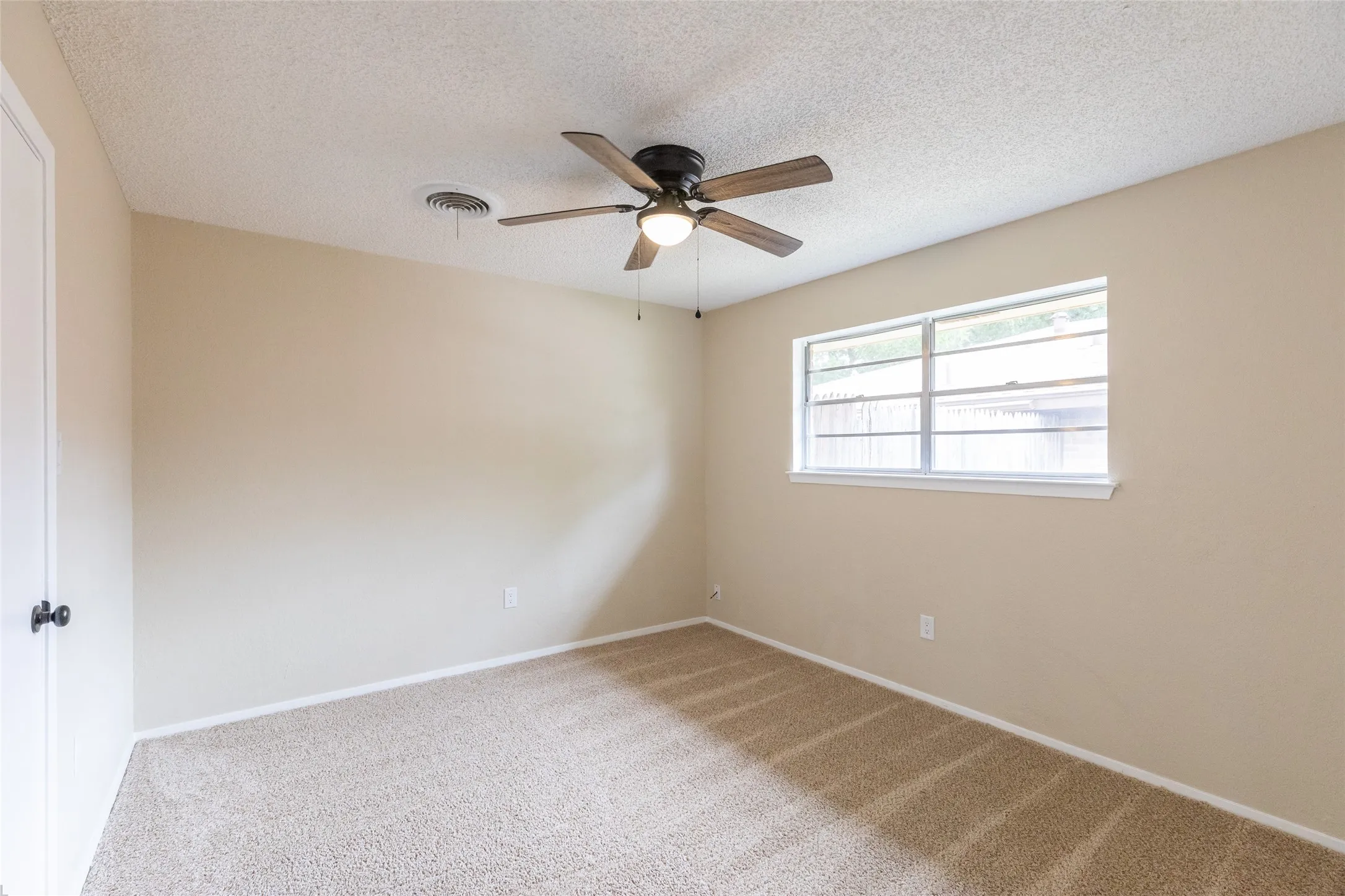Carpeted room featuring a ceiling fan with integrated lighting, a rectangular window with white trim, and a white interior door with a black knob