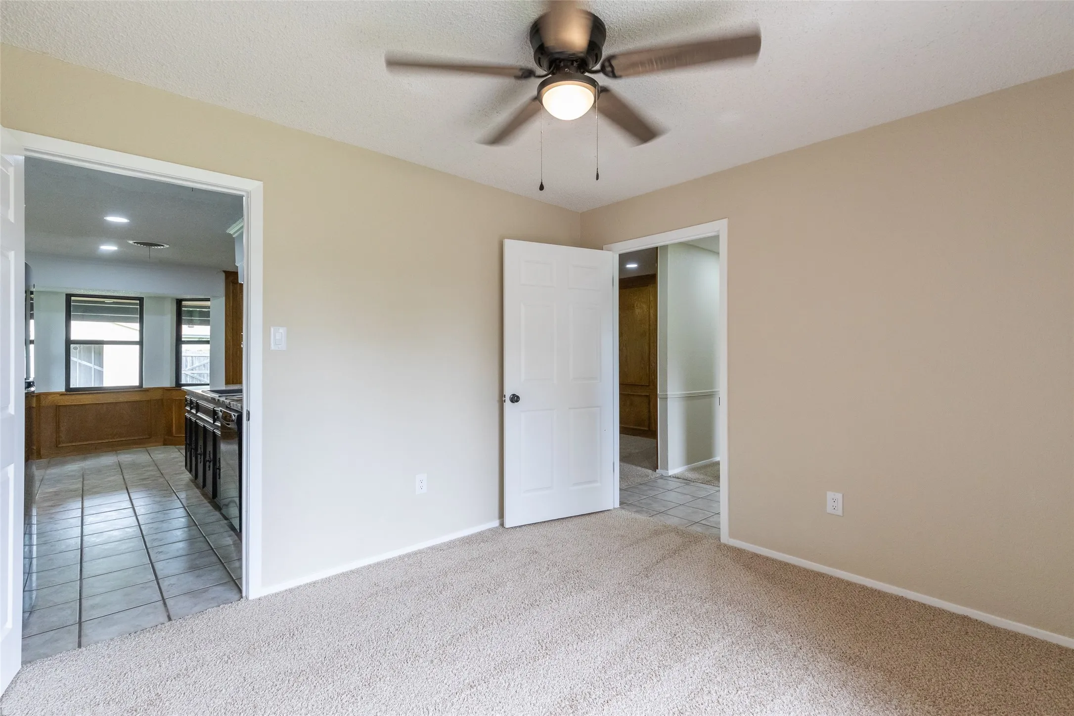 Carpeted room featuring a ceiling fan with integrated lighting, neutral wall paint, and white trim