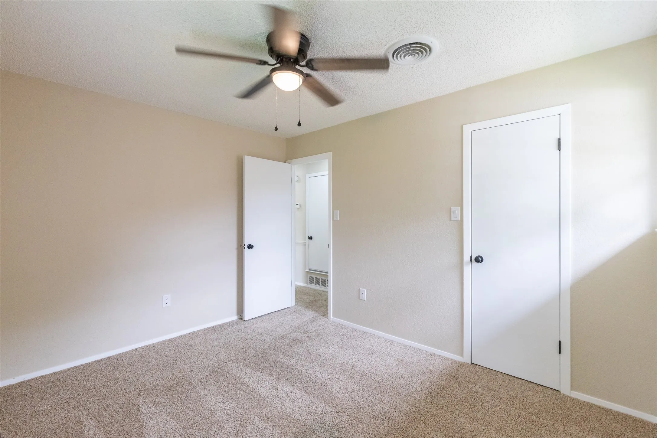 Room featuring neutral carpet flooring, light beige wall paint, white trim, and a ceiling fan with light fixture