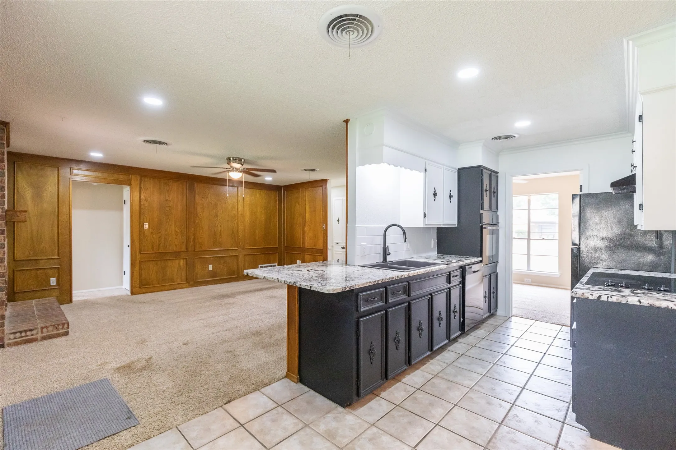 Kitchen featuring tile flooring, dark base cabinetry, white upper cabinets, and granite-patterned countertops