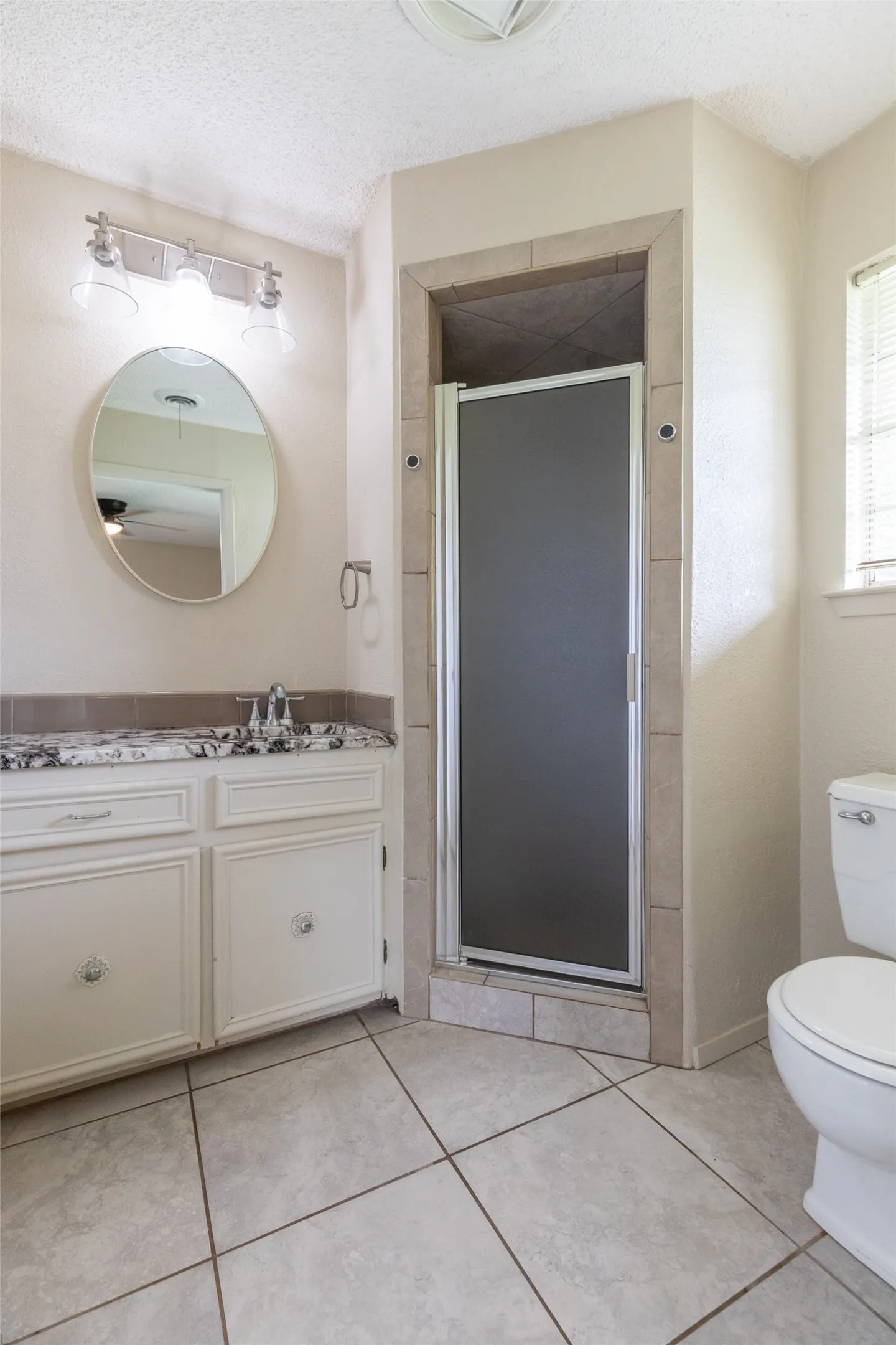 Bathroom featuring a glass-enclosed shower, single vanity with a stone-finish countertop, round mirror, and tile flooring