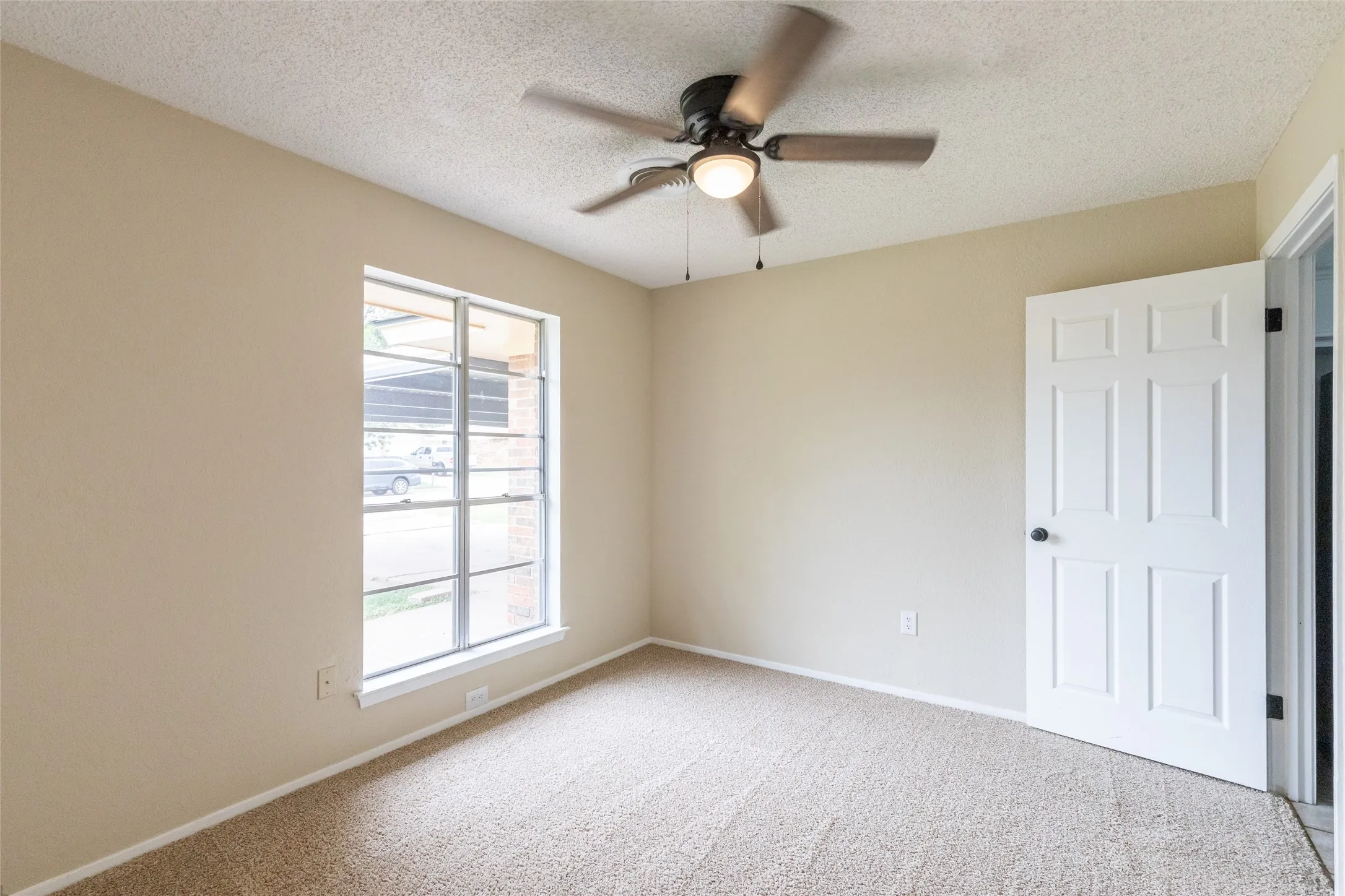 Carpeted room featuring a ceiling fan with light fixture, neutral wall paint, and a multi-pane window
