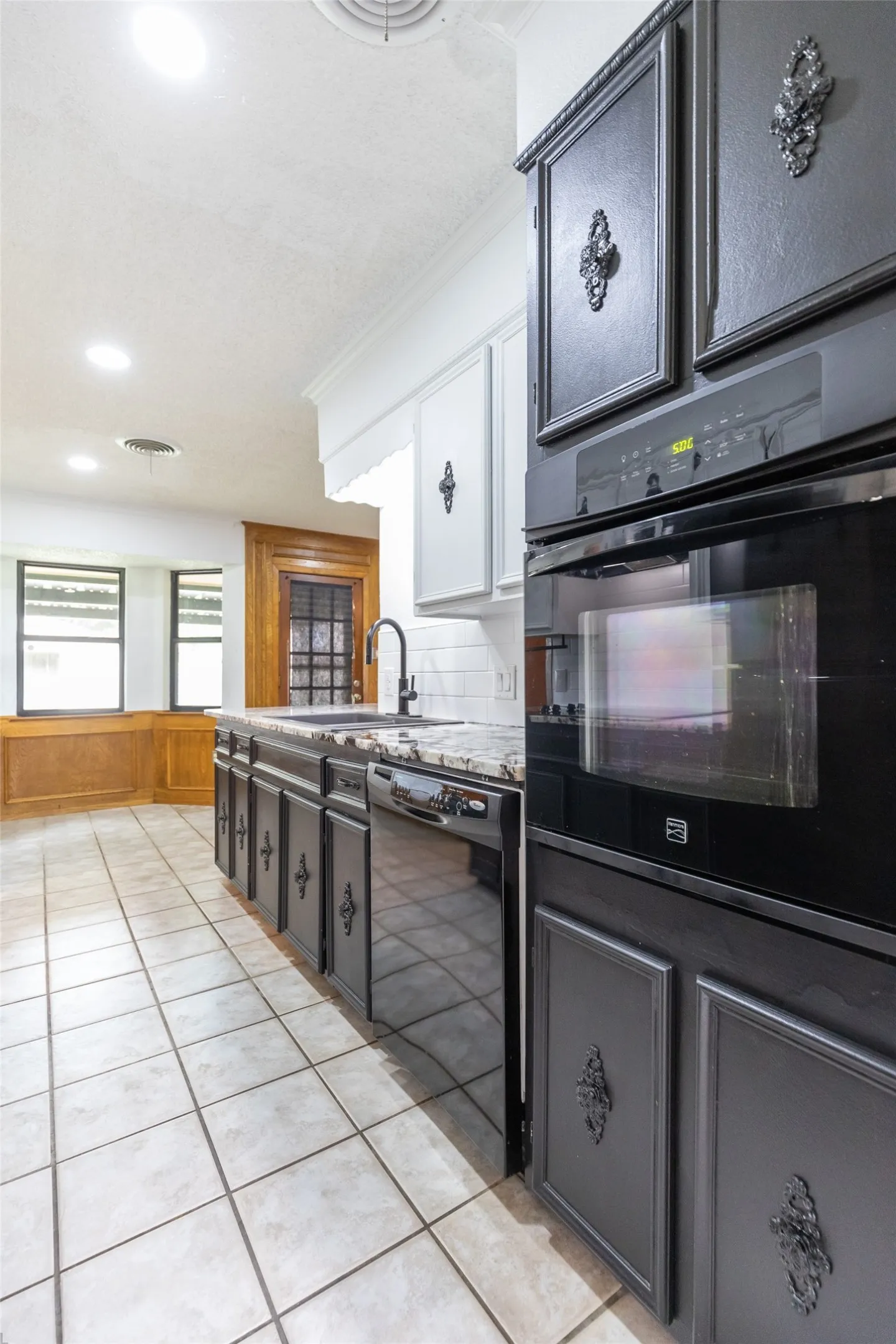 Kitchen featuring dark cabinetry, integrated wall oven, built-in microwave, and a black faucet with a white subway tile backsplash