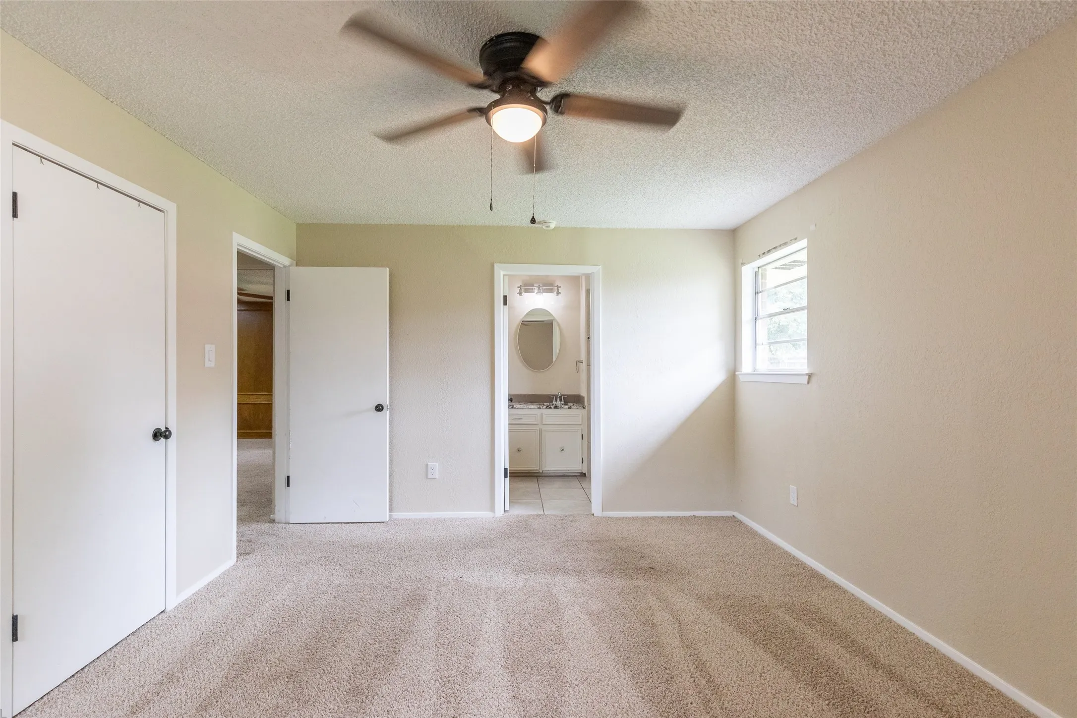 Carpeted room featuring a ceiling fan with light fixture, window with exterior views, and neutral wall tones