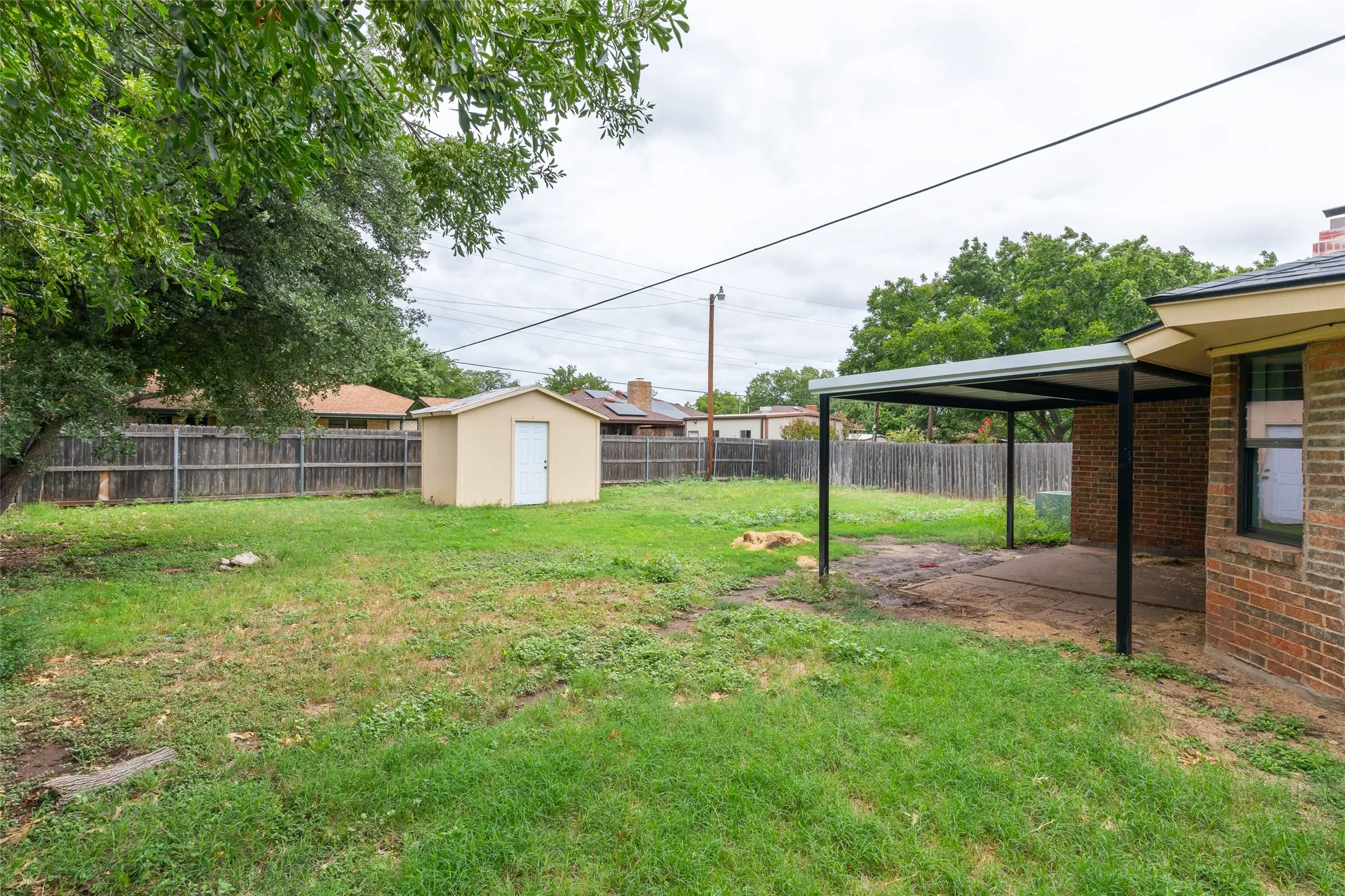 Expansive backyard featuring a detached storage shed, privacy fencing, and a covered patio area