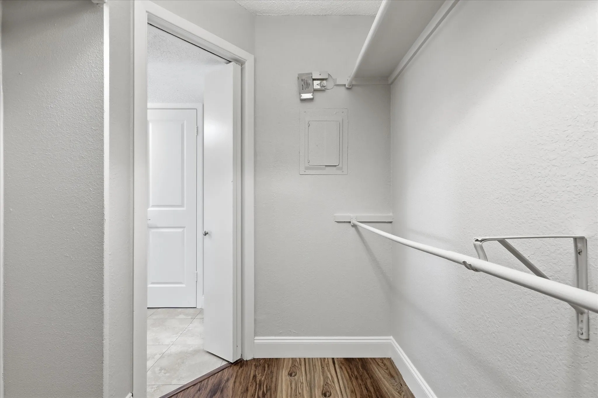Walk-in closet featuring wood-finish flooring, white walls, and a built-in hanging rod with shelving