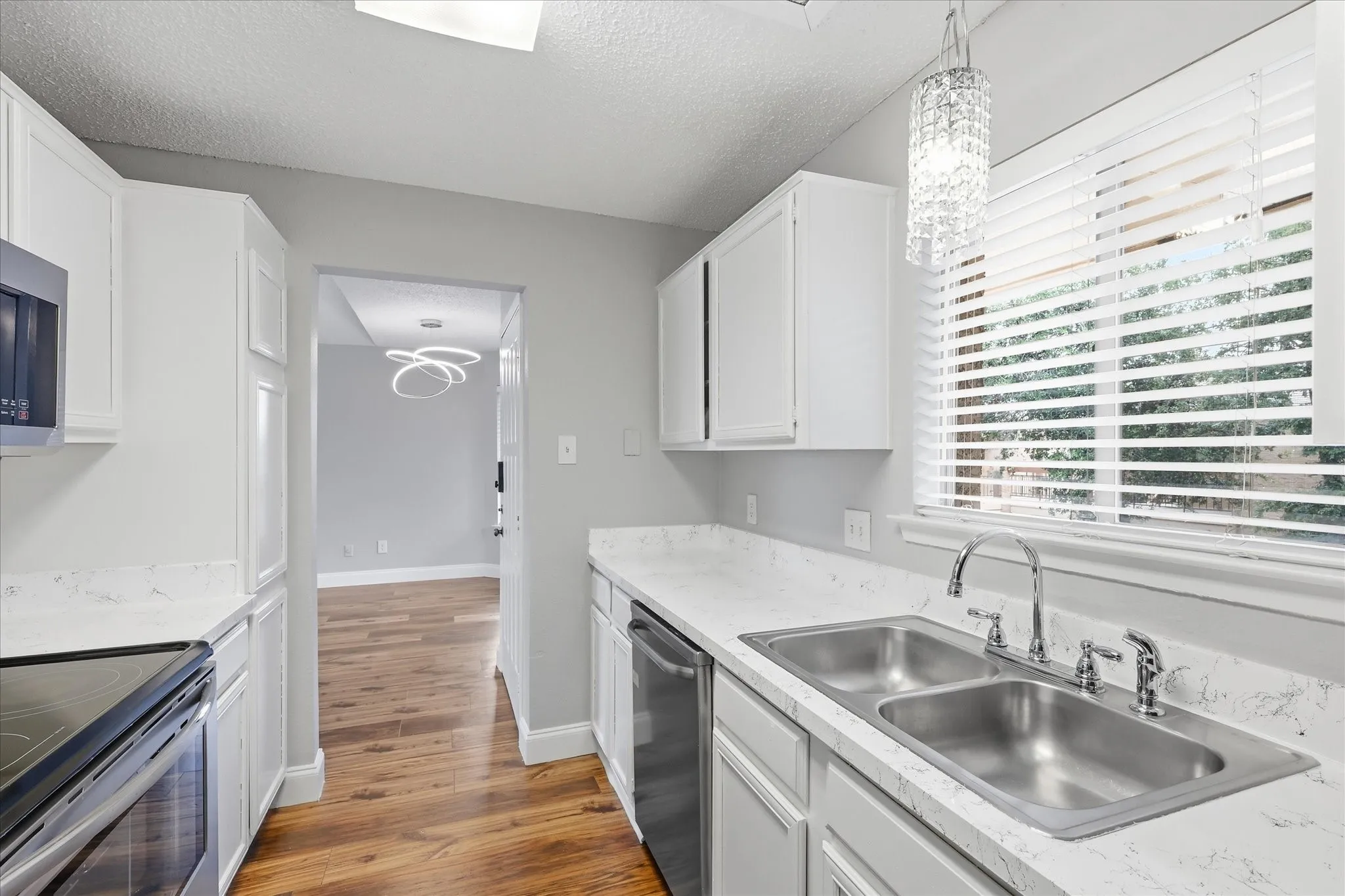 Galley-style kitchen featuring white cabinetry, light-toned countertops, a dual-basin stainless steel sink with a chrome faucet, and wood-finish flooring