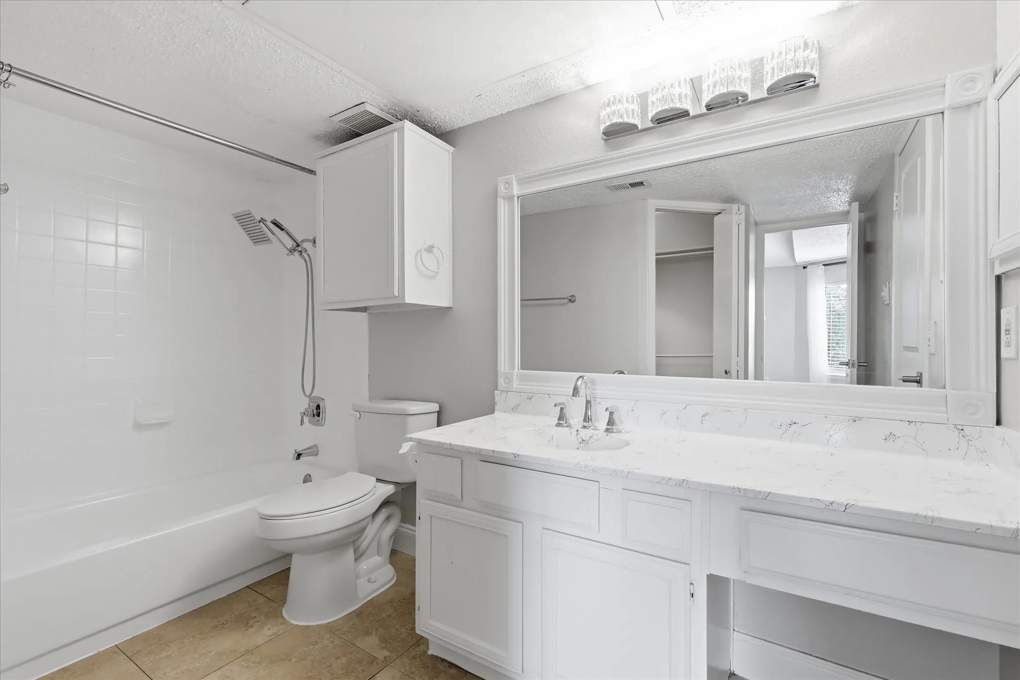 Bathroom featuring a vanity with a white countertop and integrated sink, a large wall-mounted mirror, white shaker-style cabinetry, and a tub/shower combination with white subway tile surround