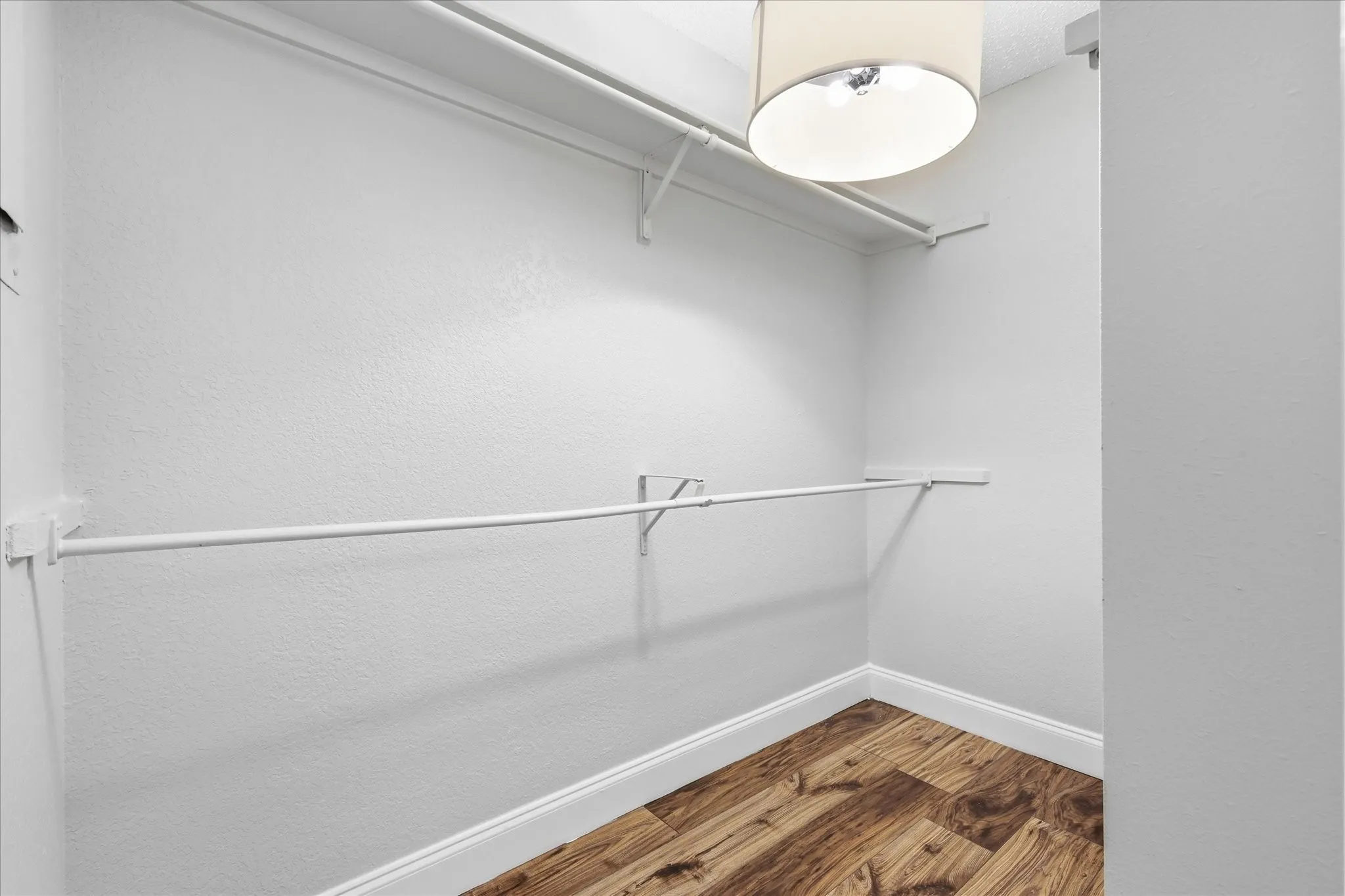 Walk-in closet featuring wood-finish flooring, white walls, built-in shelving, a hanging rod, and a ceiling-mounted light fixture