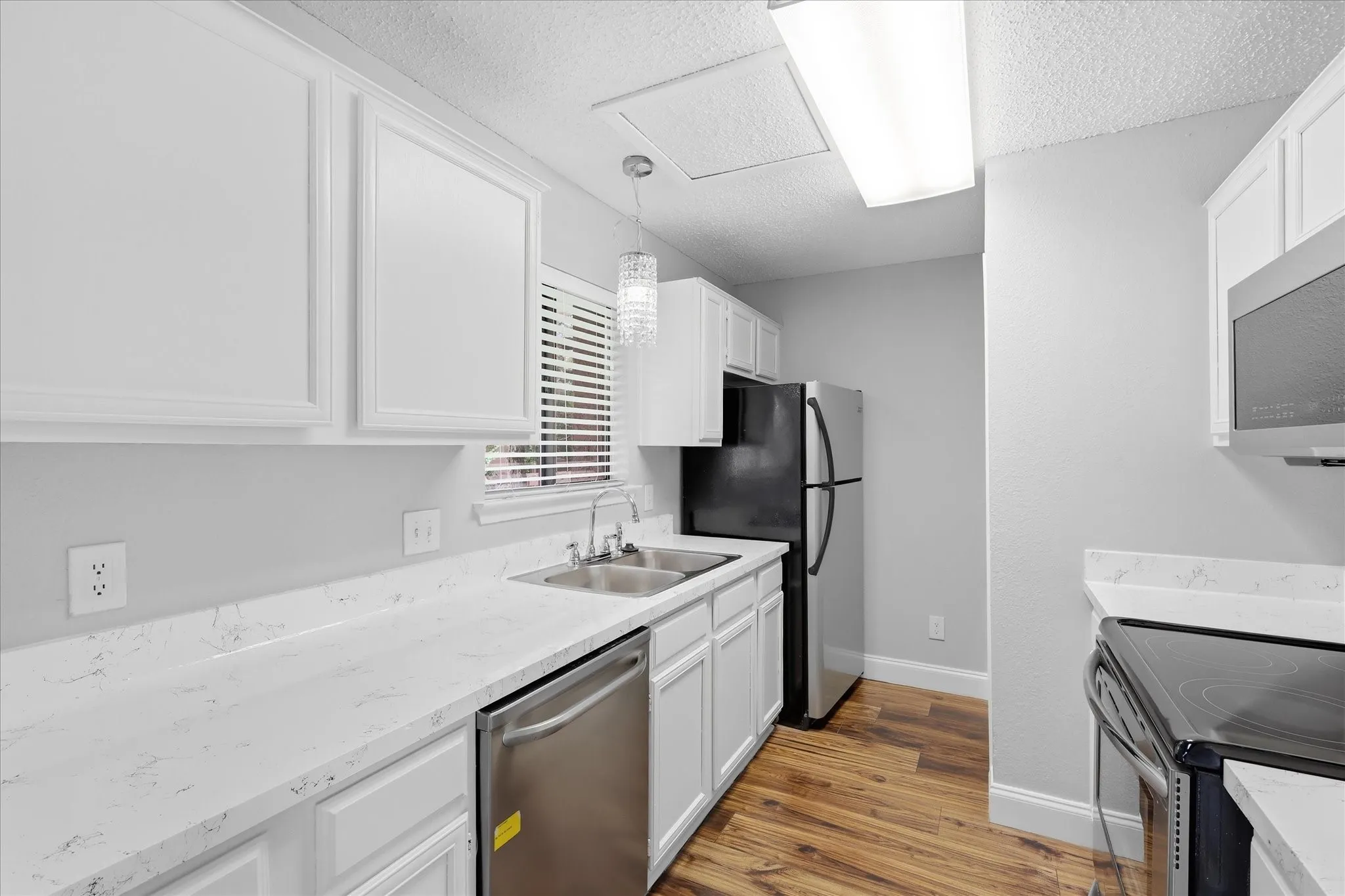 Kitchen featuring white cabinetry, light-colored countertops, stainless steel appliances, and wood-finish flooring