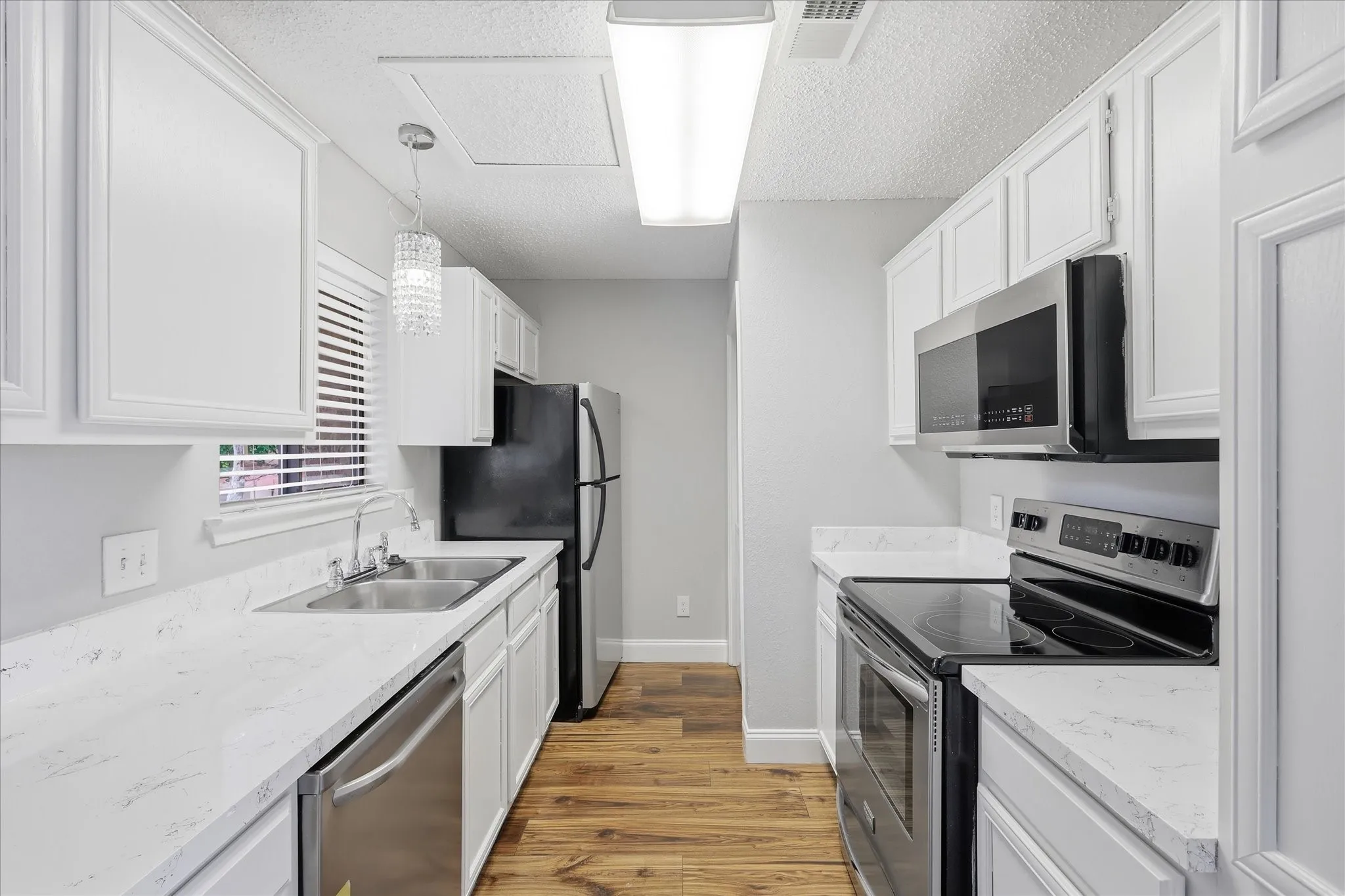 Modern galley kitchen featuring white cabinetry, light countertops, wood-finish flooring, and stainless steel appliances including a built-in microwave and dishwasher